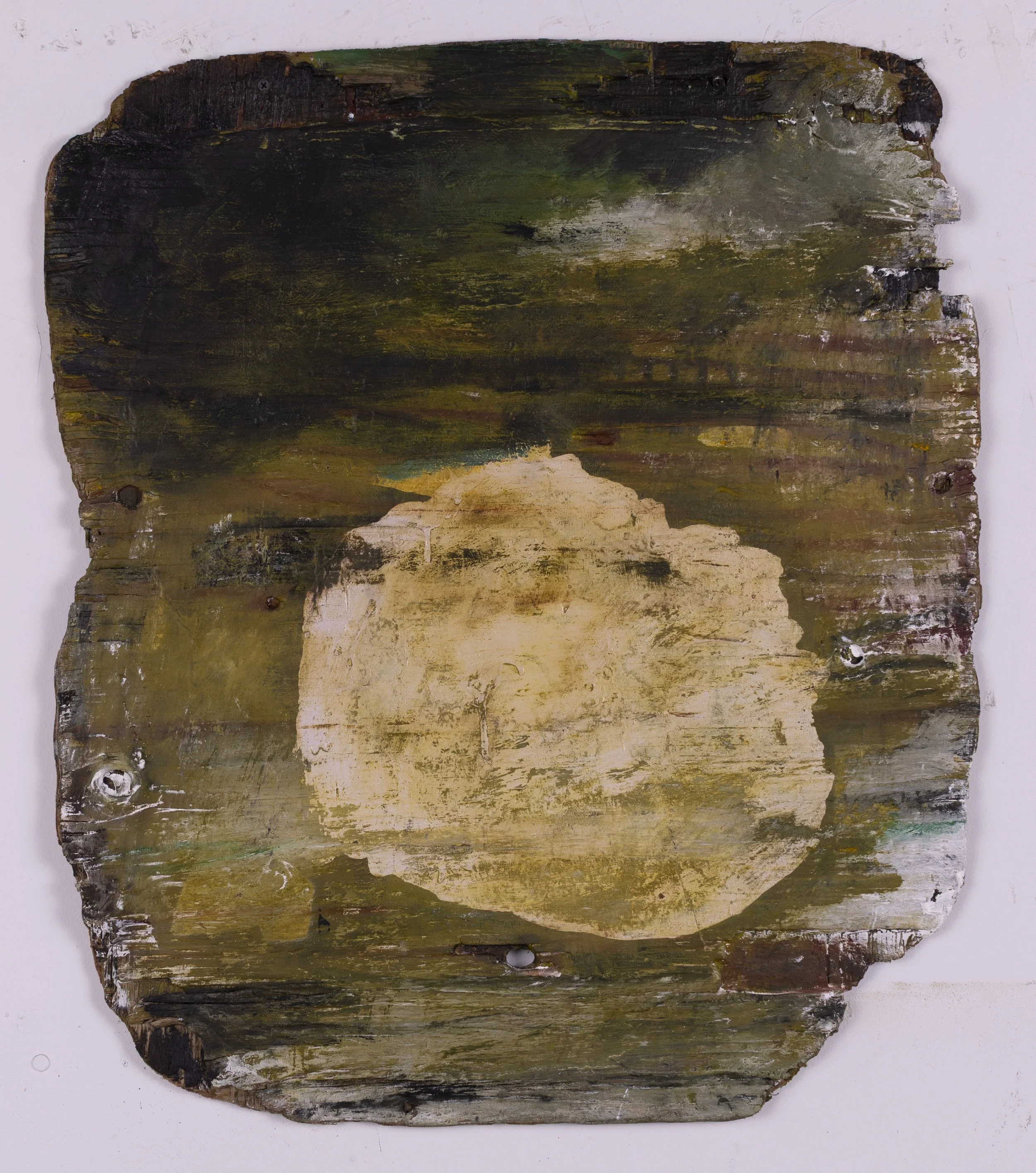 A weathered, old wooden board with remnants of paint in various shades of green, brown, and black, and a large, light-colored, roughly circular stain or patch in the center.