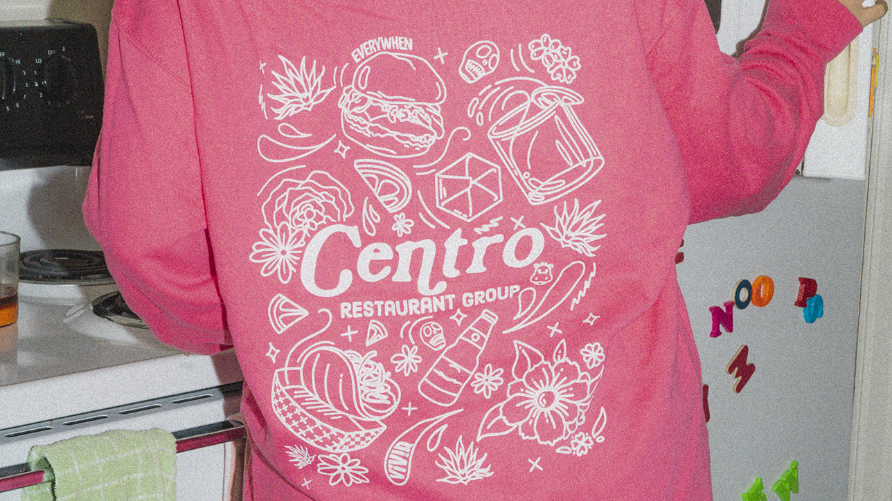A person wearing a pink sweatshirt with white cartoon illustrations and the words 'Centro Restaurant Group' in the center.