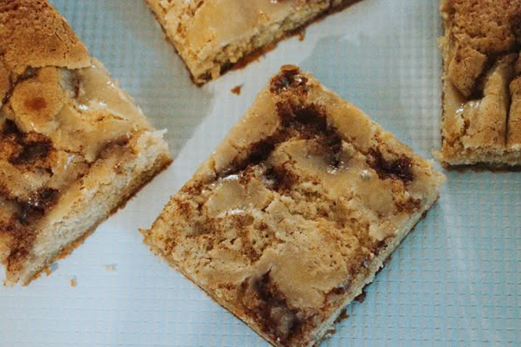 Close-up of squares of cookie bar with chocolate chips and caramel on parchment paper.