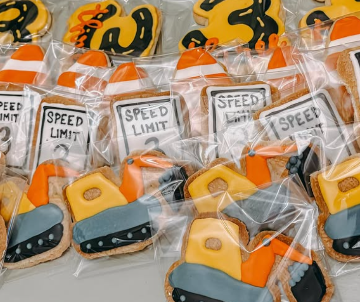 Decorated sugar cookies themed with construction zone items such as traffic cones, speed limit signs, and traffic barrels, all individually wrapped in clear plastic.