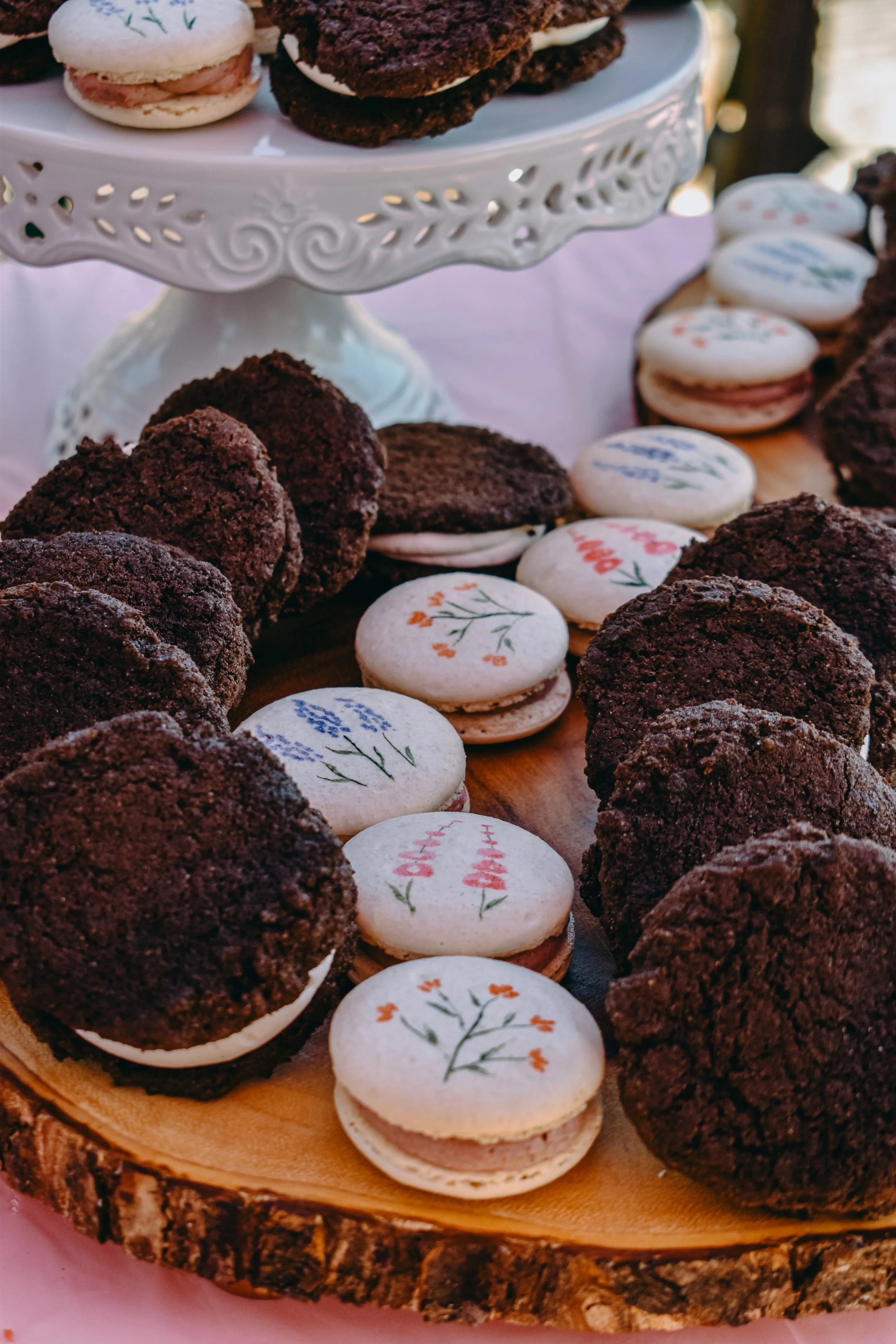 Assorted cookies and macarons arranged on a wooden serving tray and a decorative cake stand.