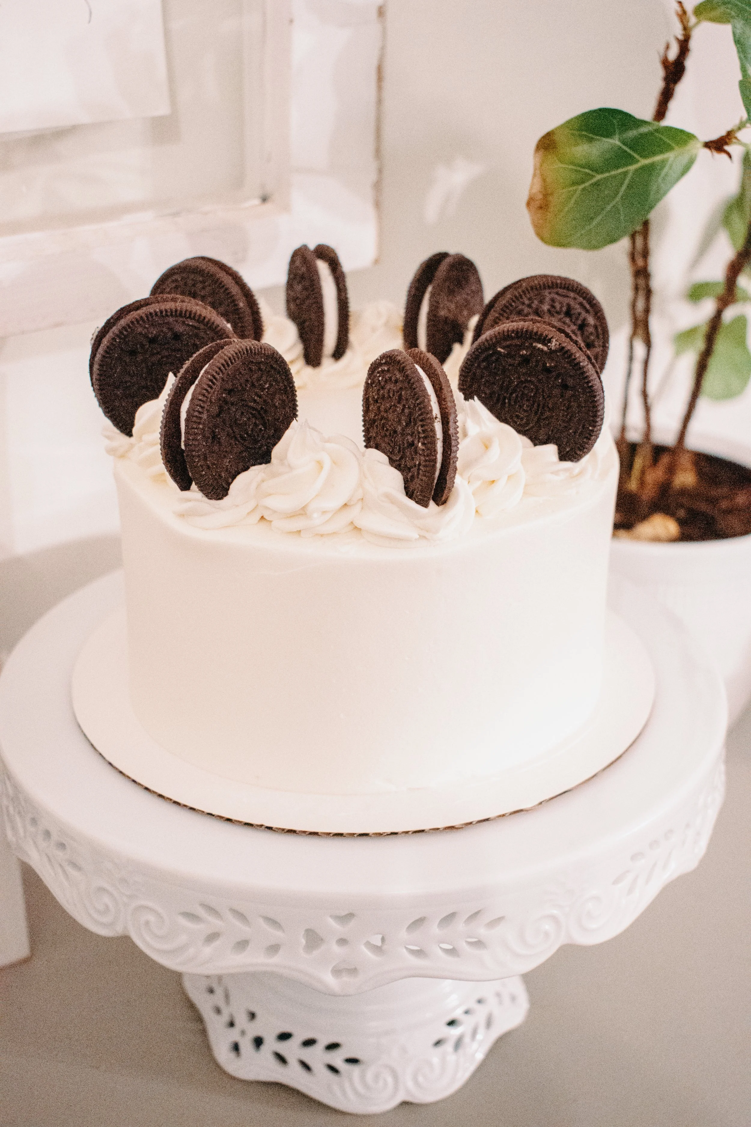White cake with Oreo cookie decorations on top, displayed on an ornate white cake stand.