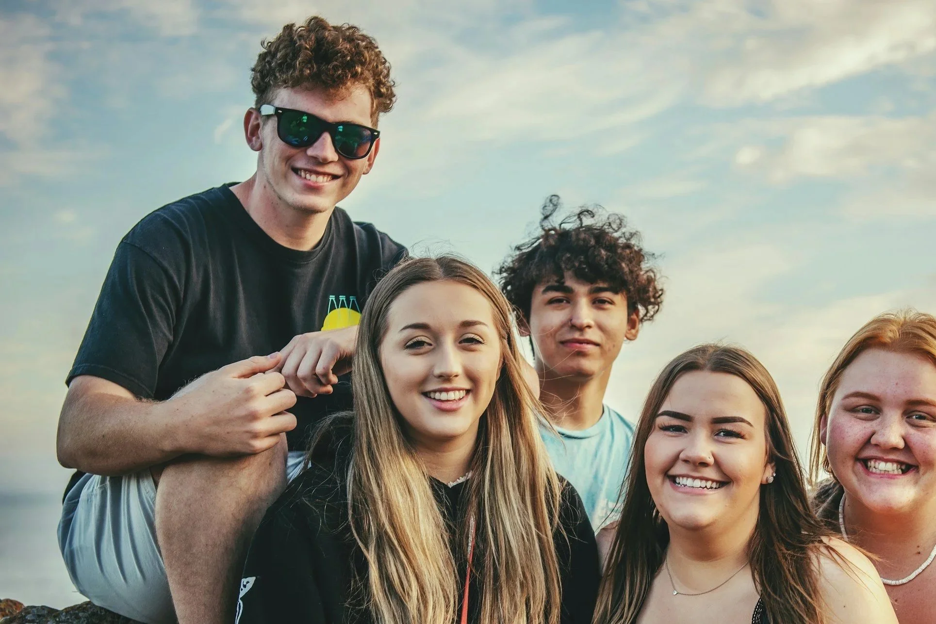 Gruppenfoto von fünf jugendlichen Freunden am Strand bei Sonnenuntergang.