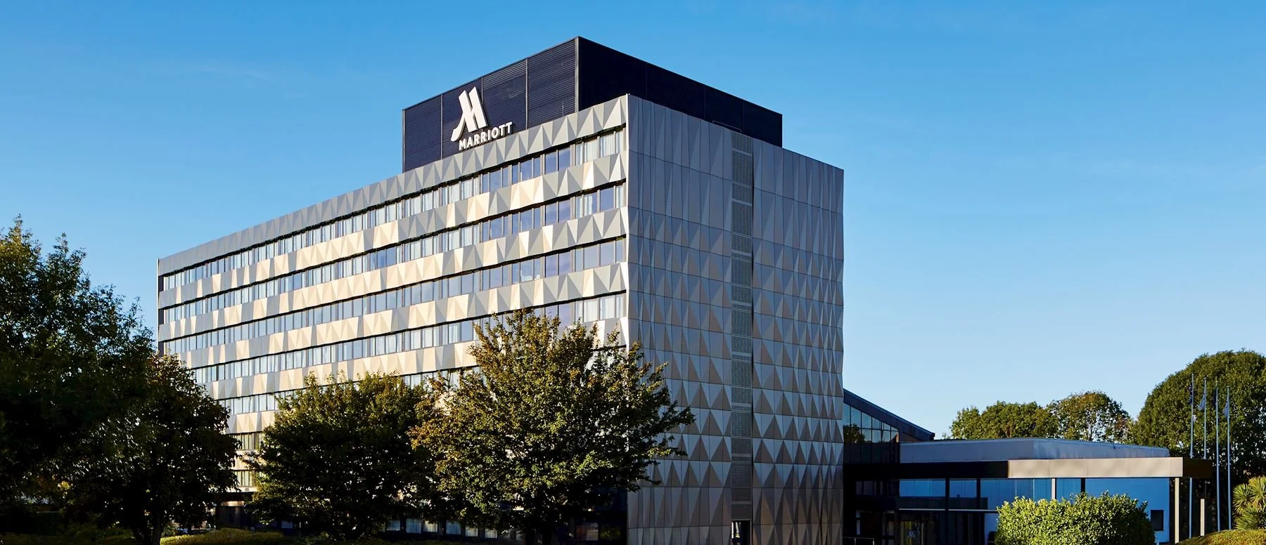 Modern hotel building with the Marriott logo on top, surrounded by trees and a clear blue sky.