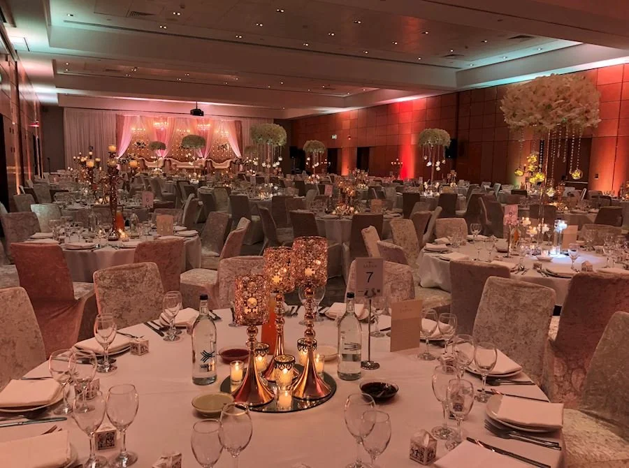 Elegant banquet hall decorated for a wedding or formal event with round tables, floral centerpieces, candles, and soft lighting.