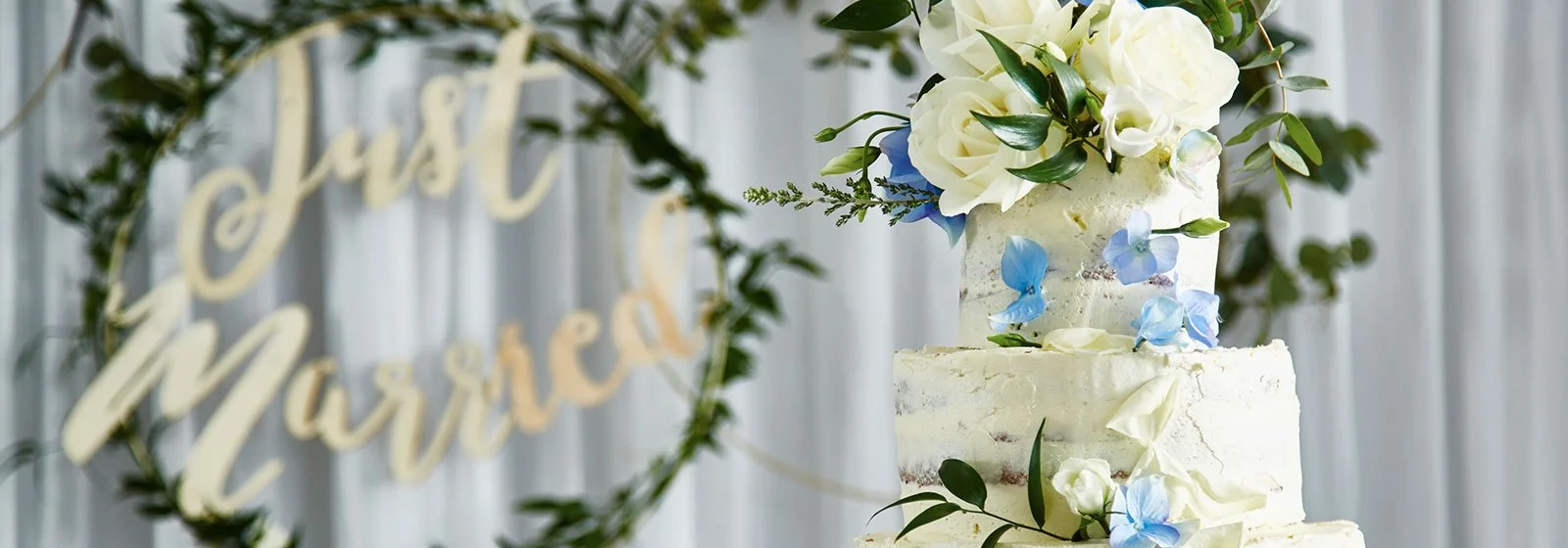 A three-tiered wedding cake decorated with white roses and blue butterflies.