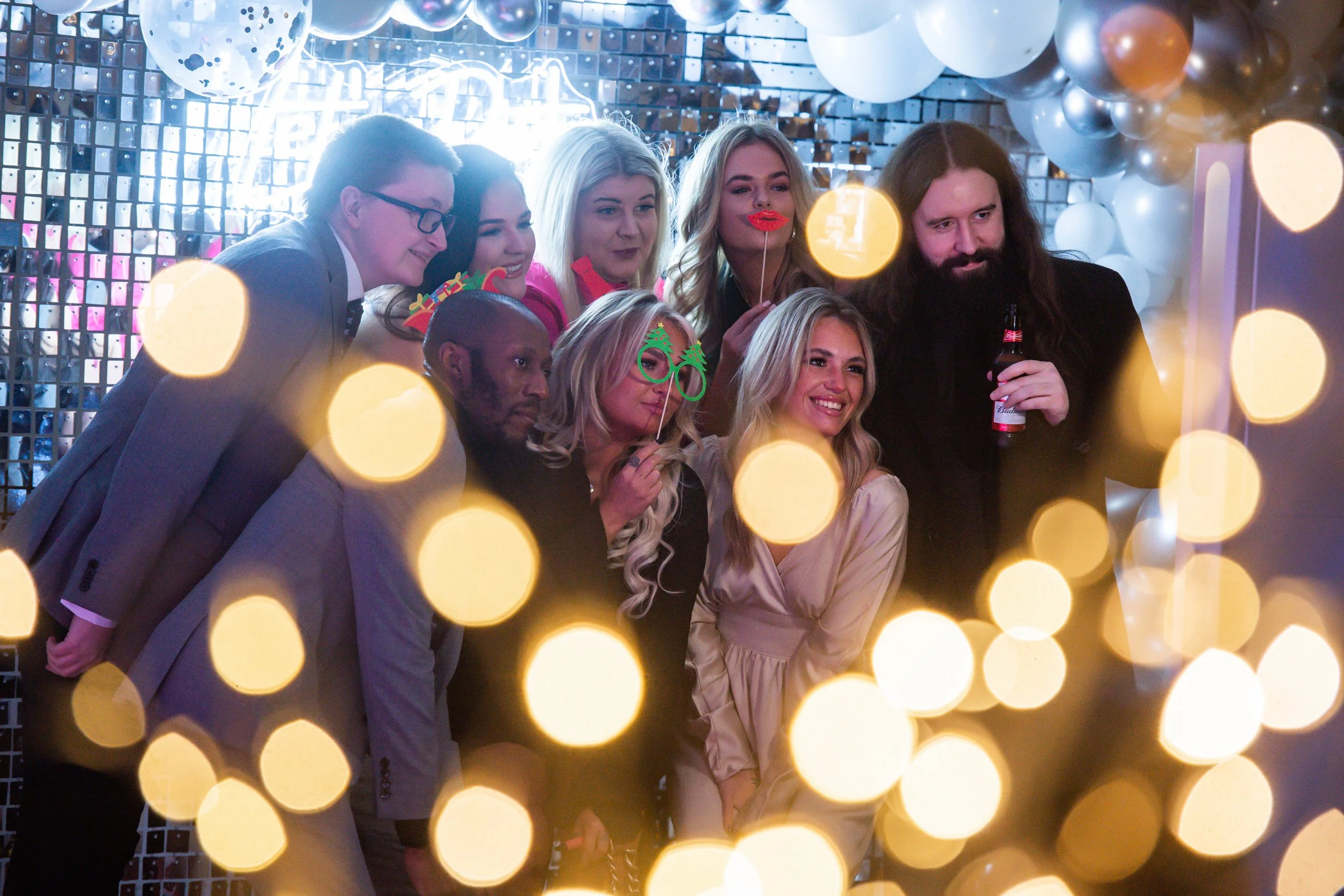 Group of people at a party taking a photo with bright lights and balloons in the background.
