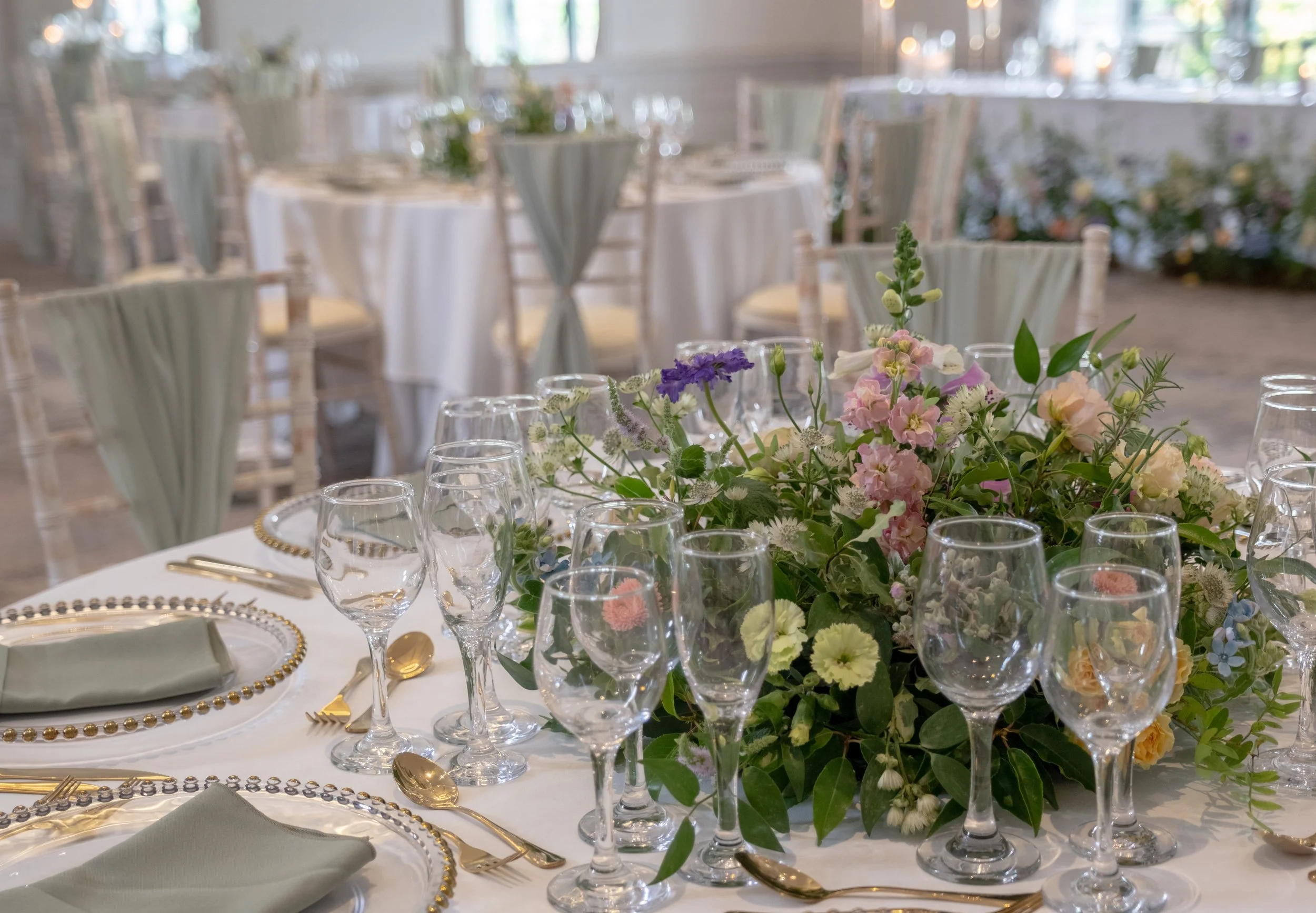 Elegant banquet table with a floral centerpiece, surrounded by glasses, gold utensils, and decorated plates in a well-lit room.