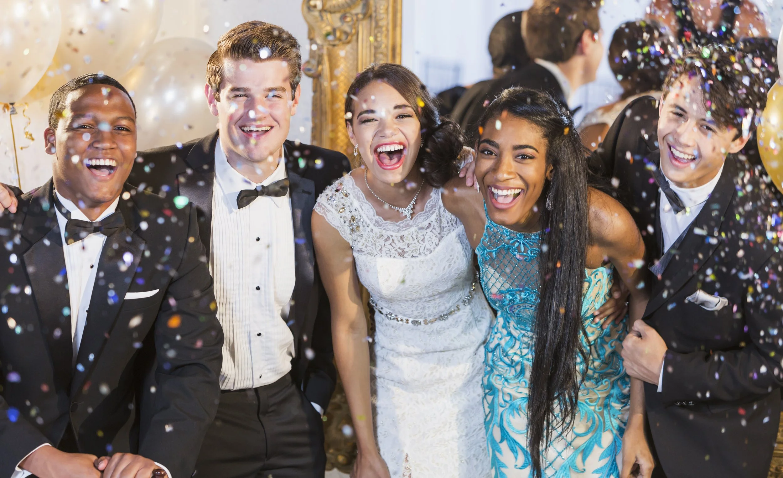Group of young adults at a celebration, wearing formal attire, smiling, with confetti falling around them.