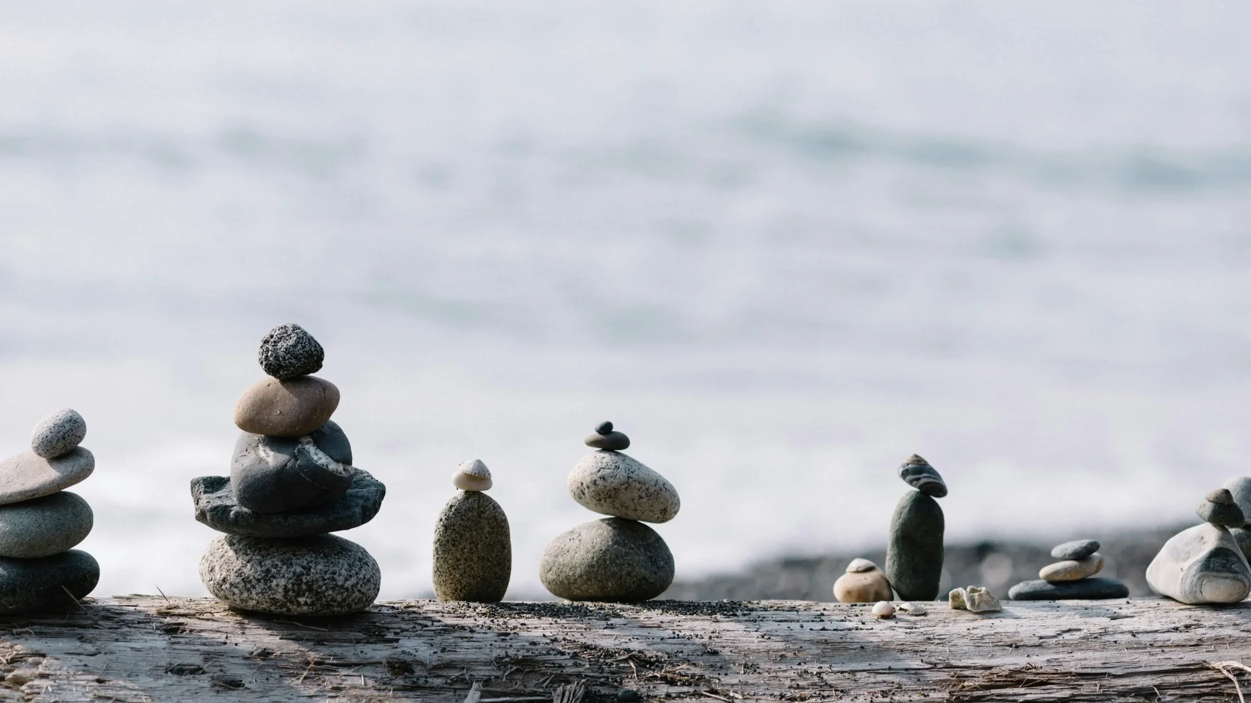 Several stacks of smooth stones arranged on a wooden surface against a blurred ocean background.