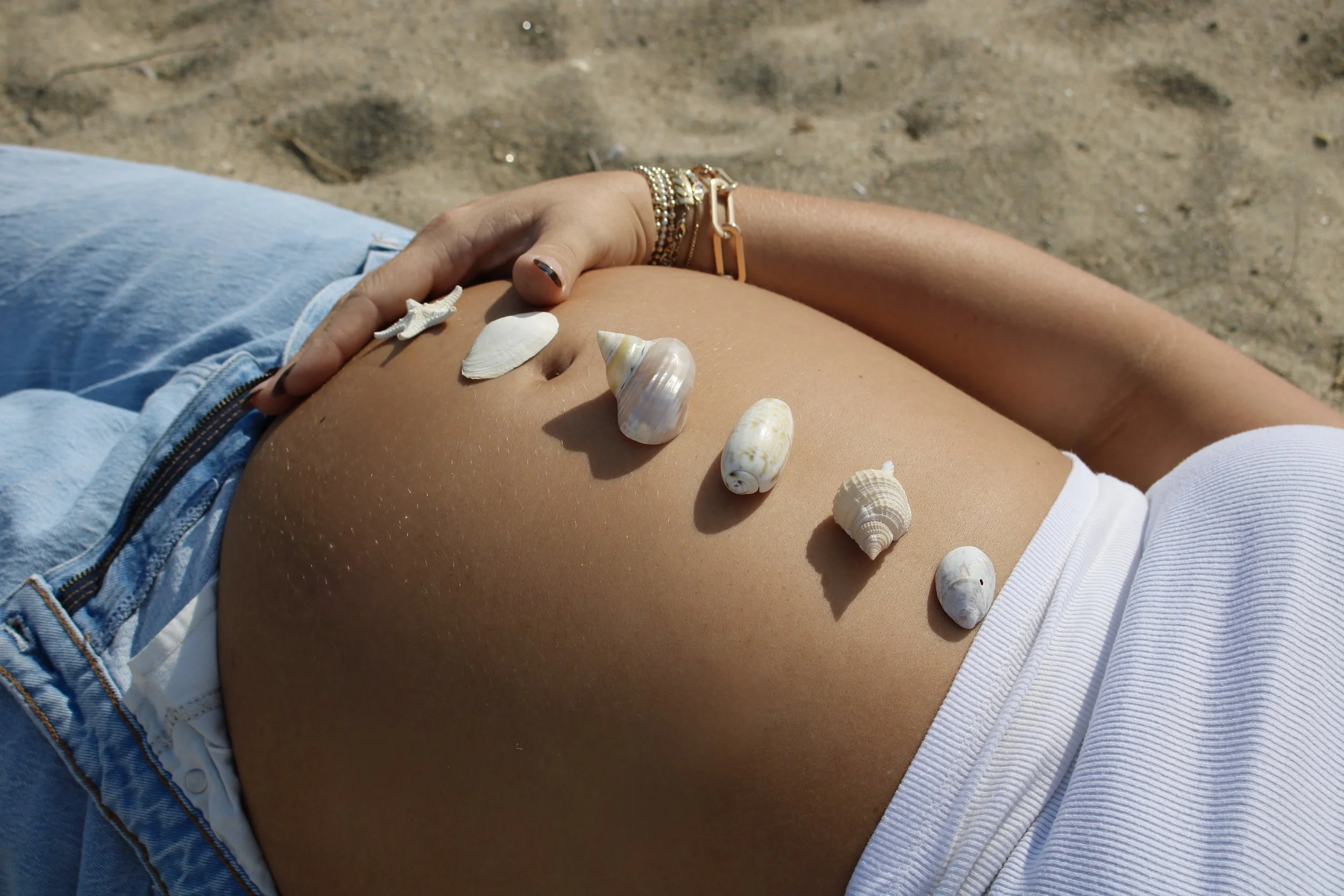 A pregnant woman lying on the beach with seashells placed on her belly