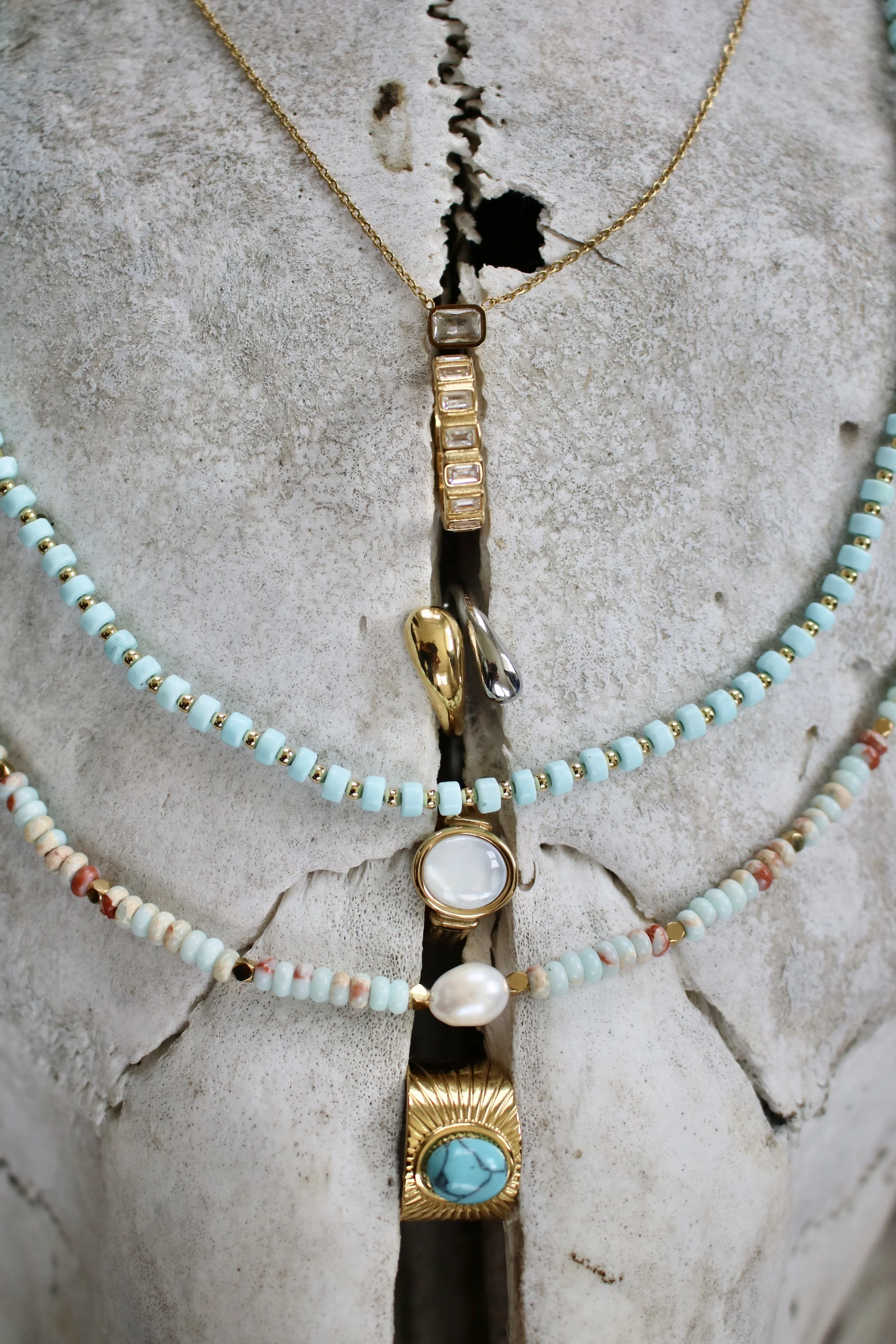 Multiple layered necklaces with beads and pendants, displayed on a textured stone background.
