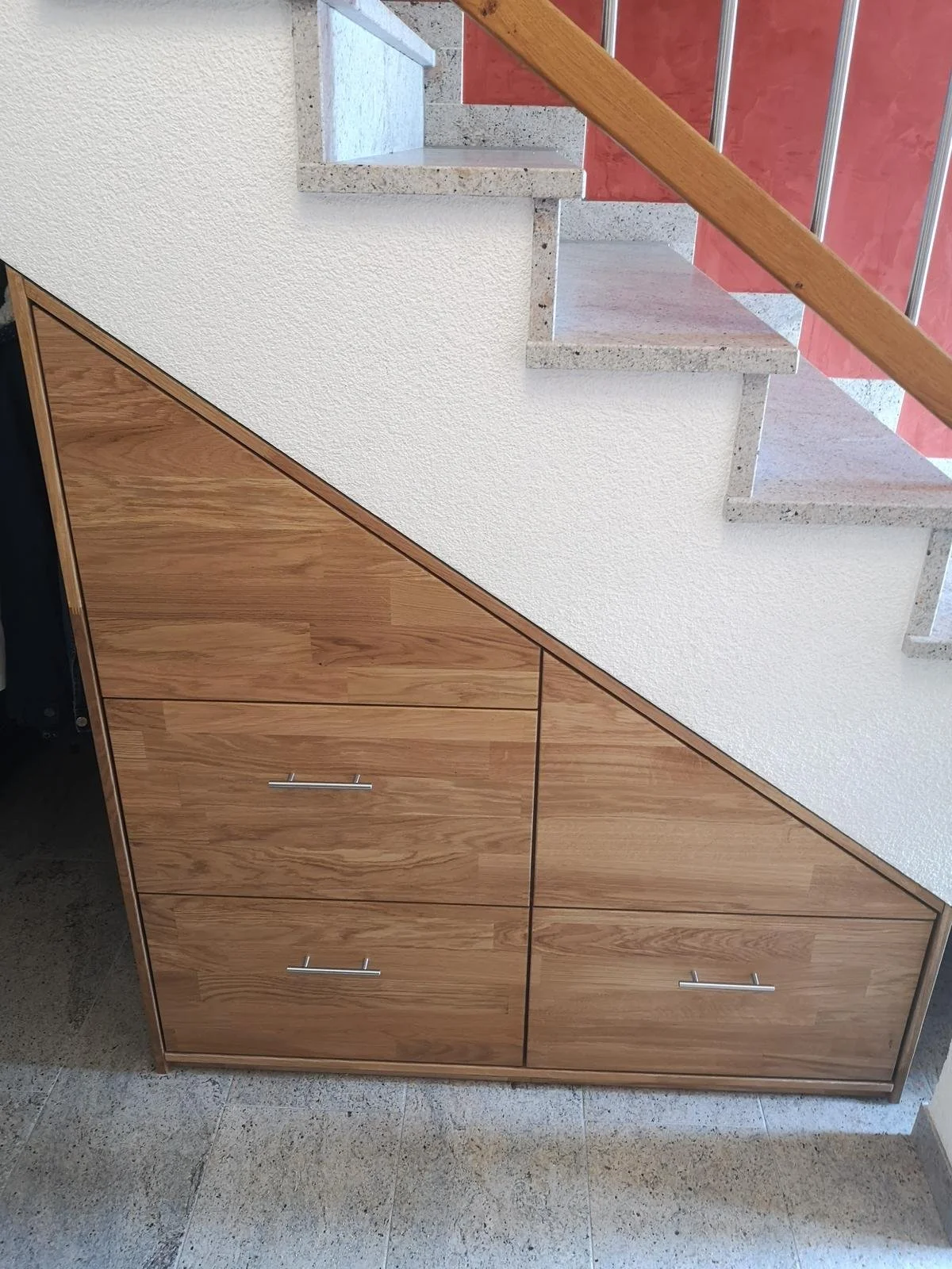 Holzkast under einer Treppe mit Handgriffen, auf dem eine Jacke hängt.