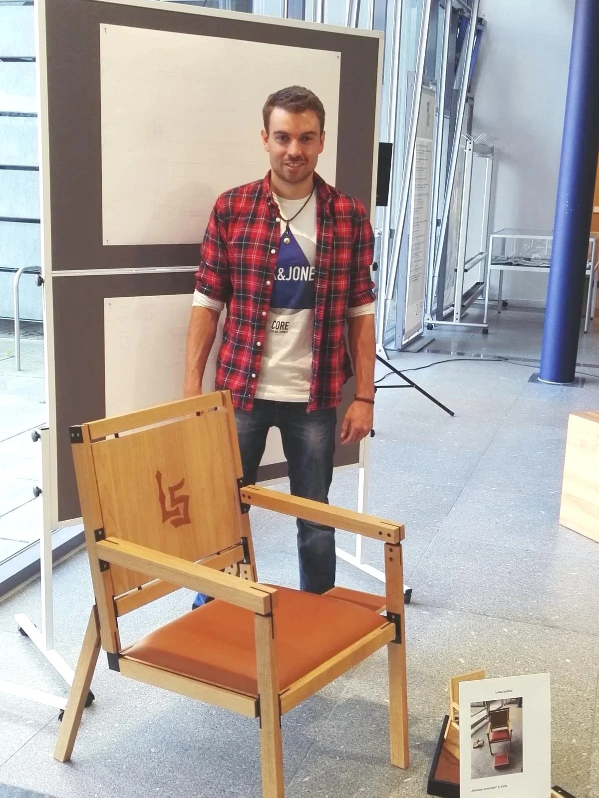 Ein junger Mann steht hinter einem Holzsessel mit Swastika-Logo, der bei einer Ausstellung gezeigt wird.