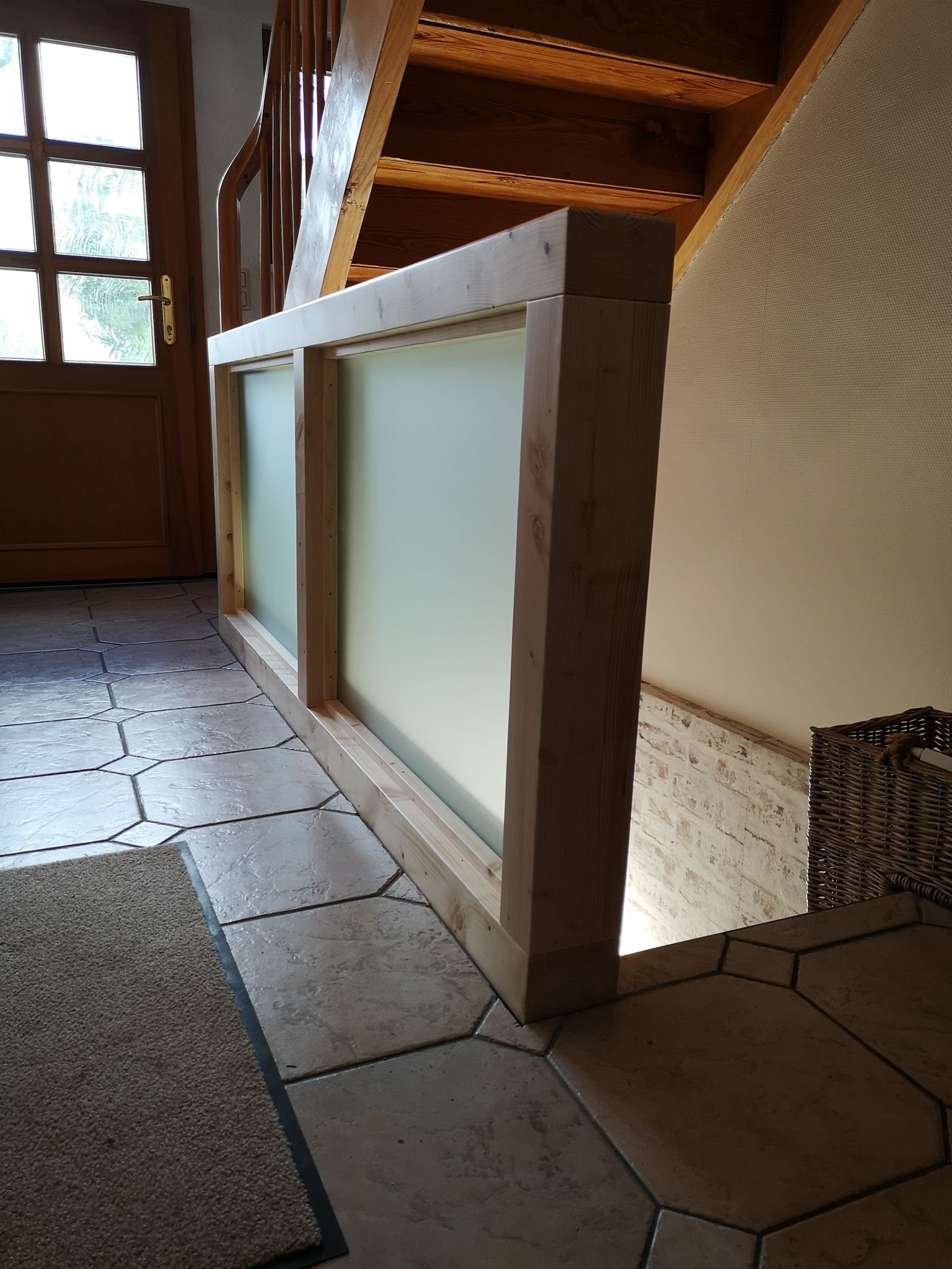 Ein Holzgeländer mit beleuchteter, lichtgrüner Glaseinfassung im Flur eines Hauses, mit Terrassentür im Hintergrund.