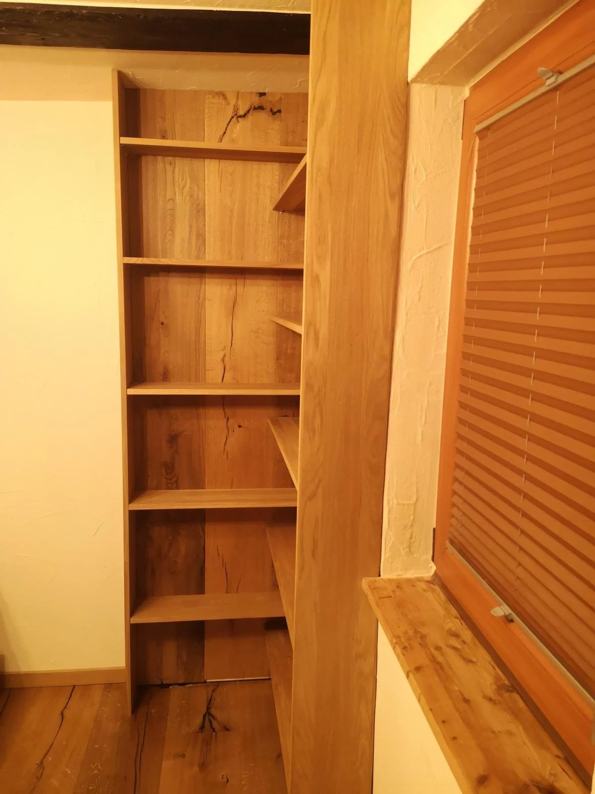 Leeres Holzregal in einem Raum mit Holzfußboden und Fenster mit Rollladen.