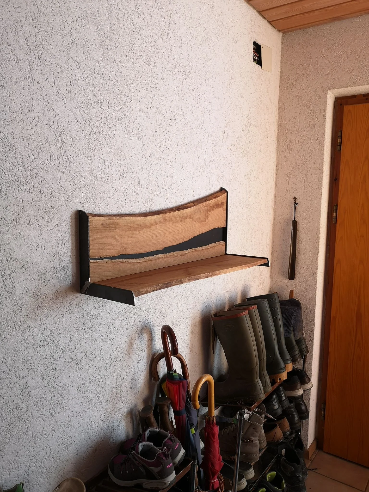 Wand mit einer Holzbank und einer Schuhablage mit verschiedenen Schuhen und Gummistiefeln, sowie einen Regenschirm und andere Utensilien.