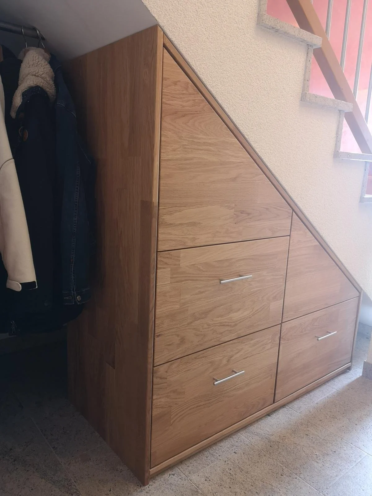 Holzkast under einer Treppe mit Handgriffen, auf dem eine Jacke hängt.