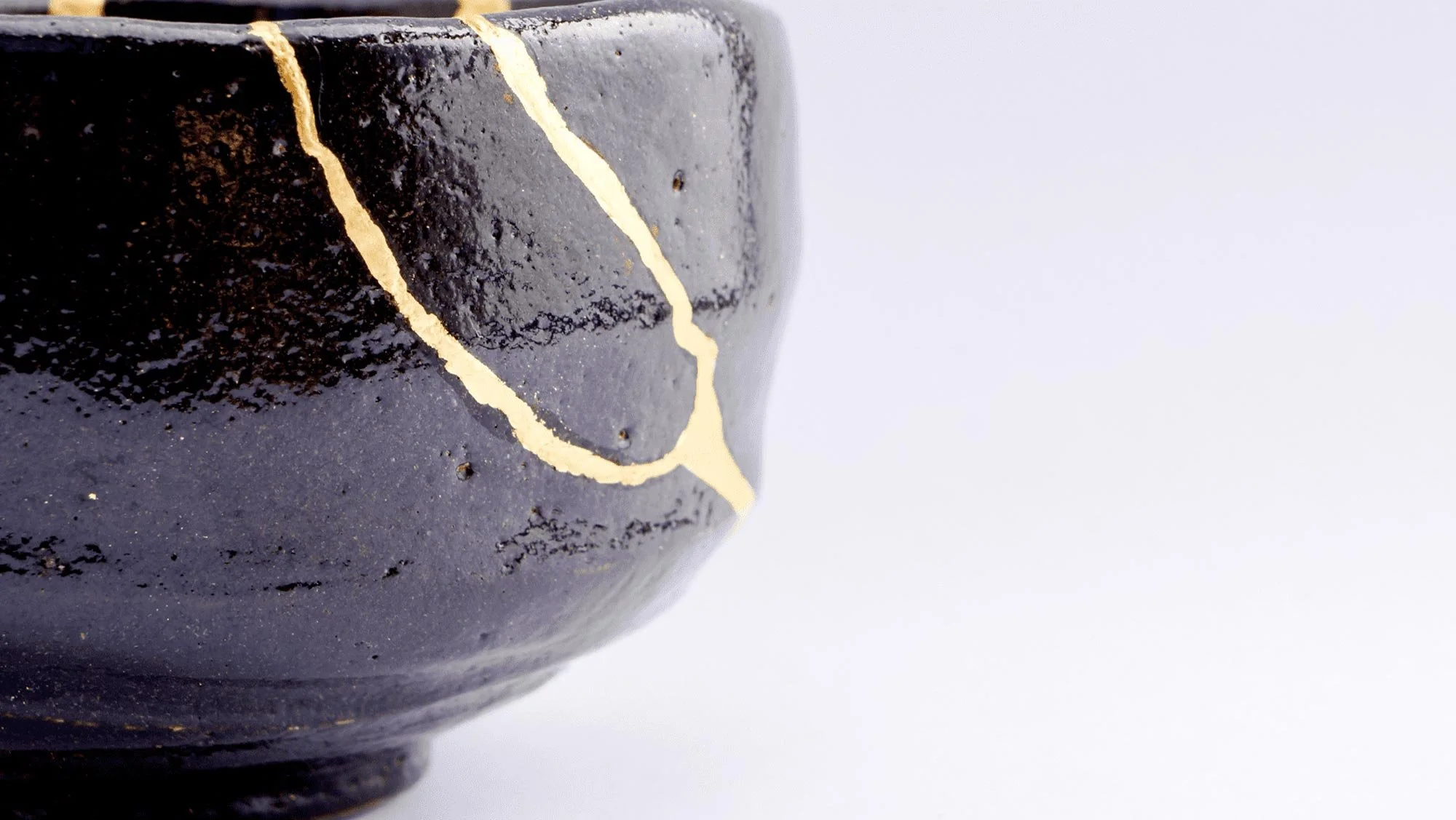 Close-up of a black ceramic bowl with golden cracks on its surface against a white background.