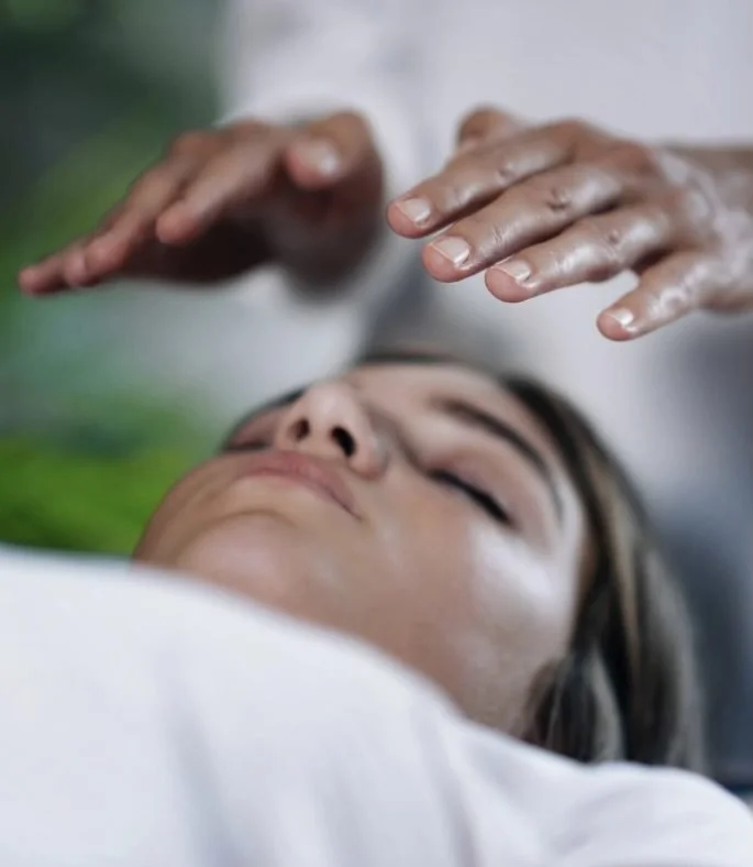 A person receiving a massage or healing treatment with hands hovering above their face while lying down.