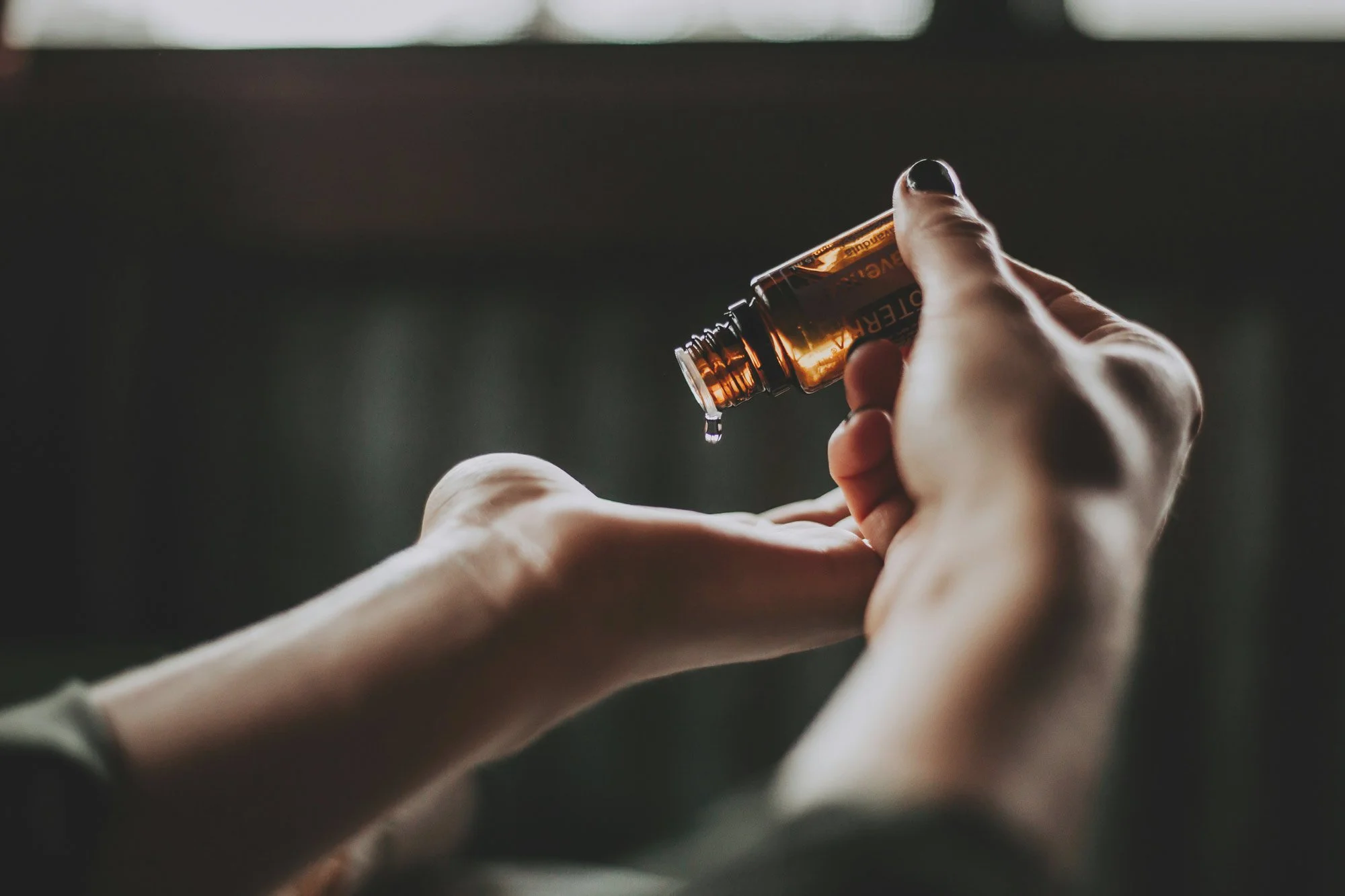 A person is pouring a liquid from a small amber glass bottle into their hand.