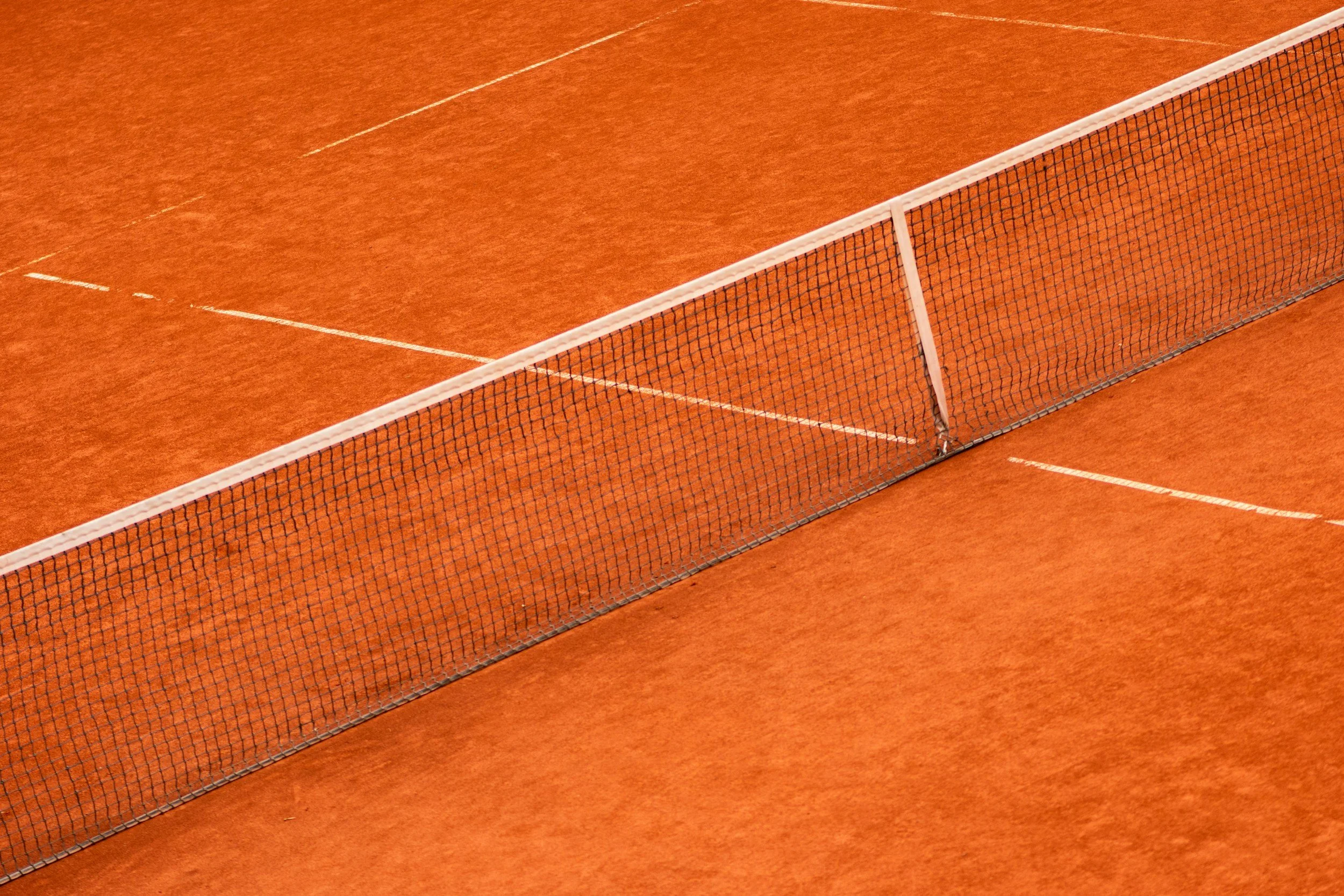 Ansicht eines Tennisplatzes mit roter Oberfläche und halbhohem Netz.