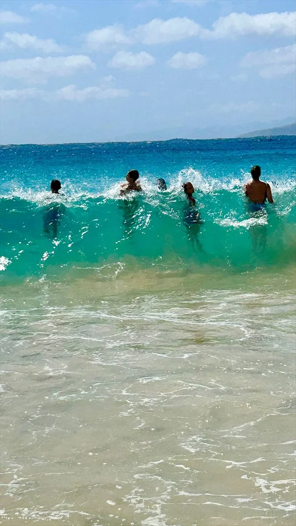 Group of five people enjoying the ocean waves at the beach with blue sky and clouds above.