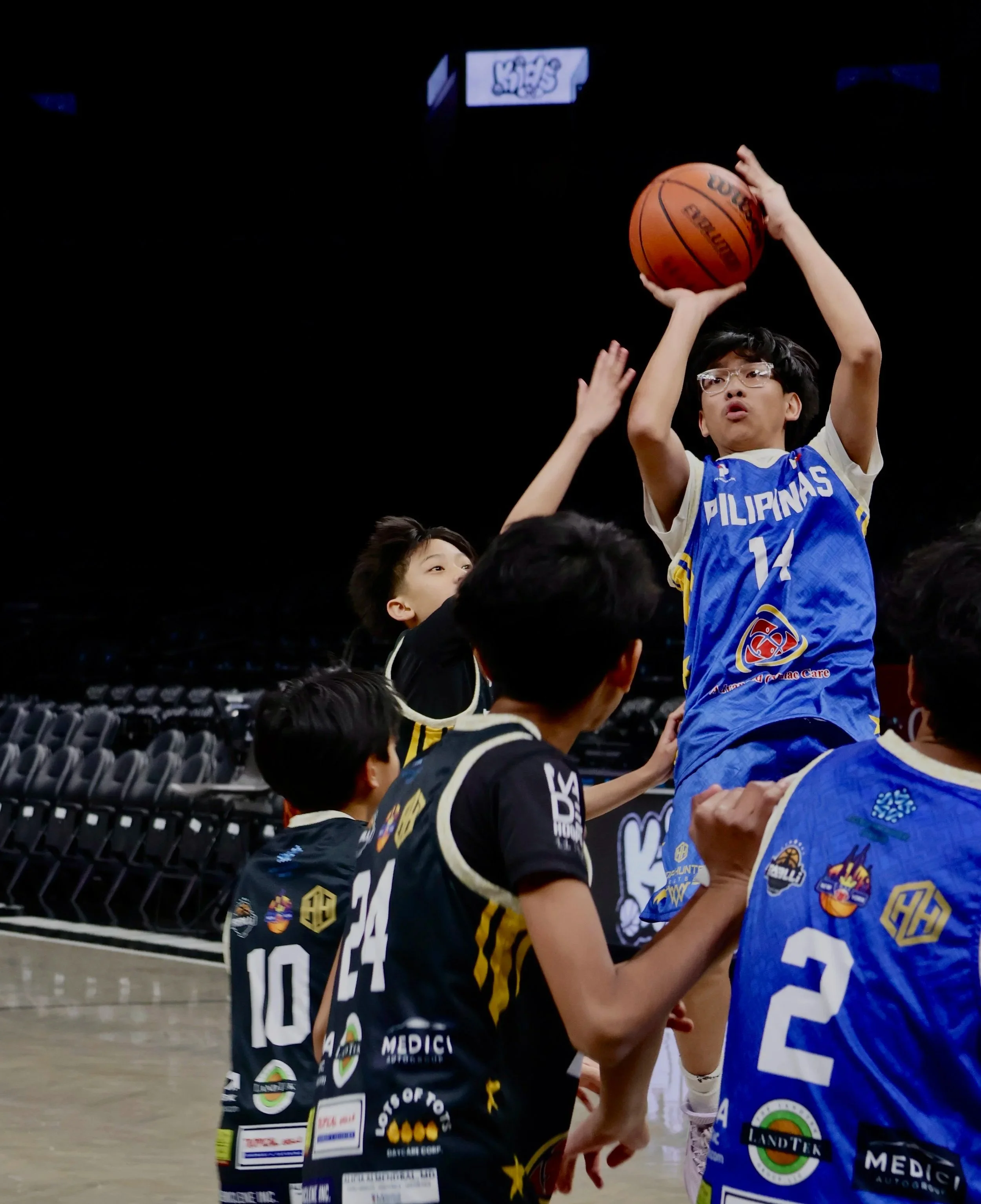 Young basketball players in uniforms competing for the ball during a game in an indoor arena.