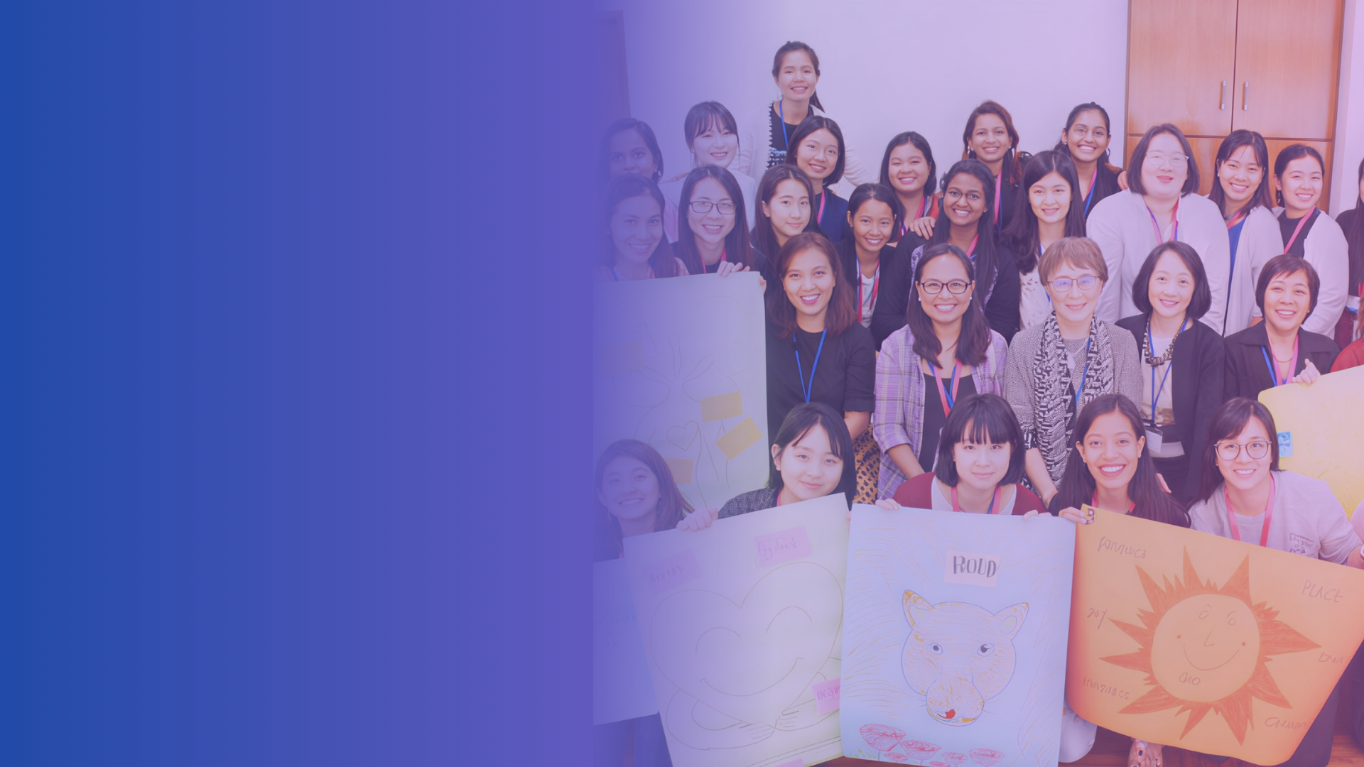 Group of children and adults holding colorful drawings and posters, smiling in a classroom or event setting.