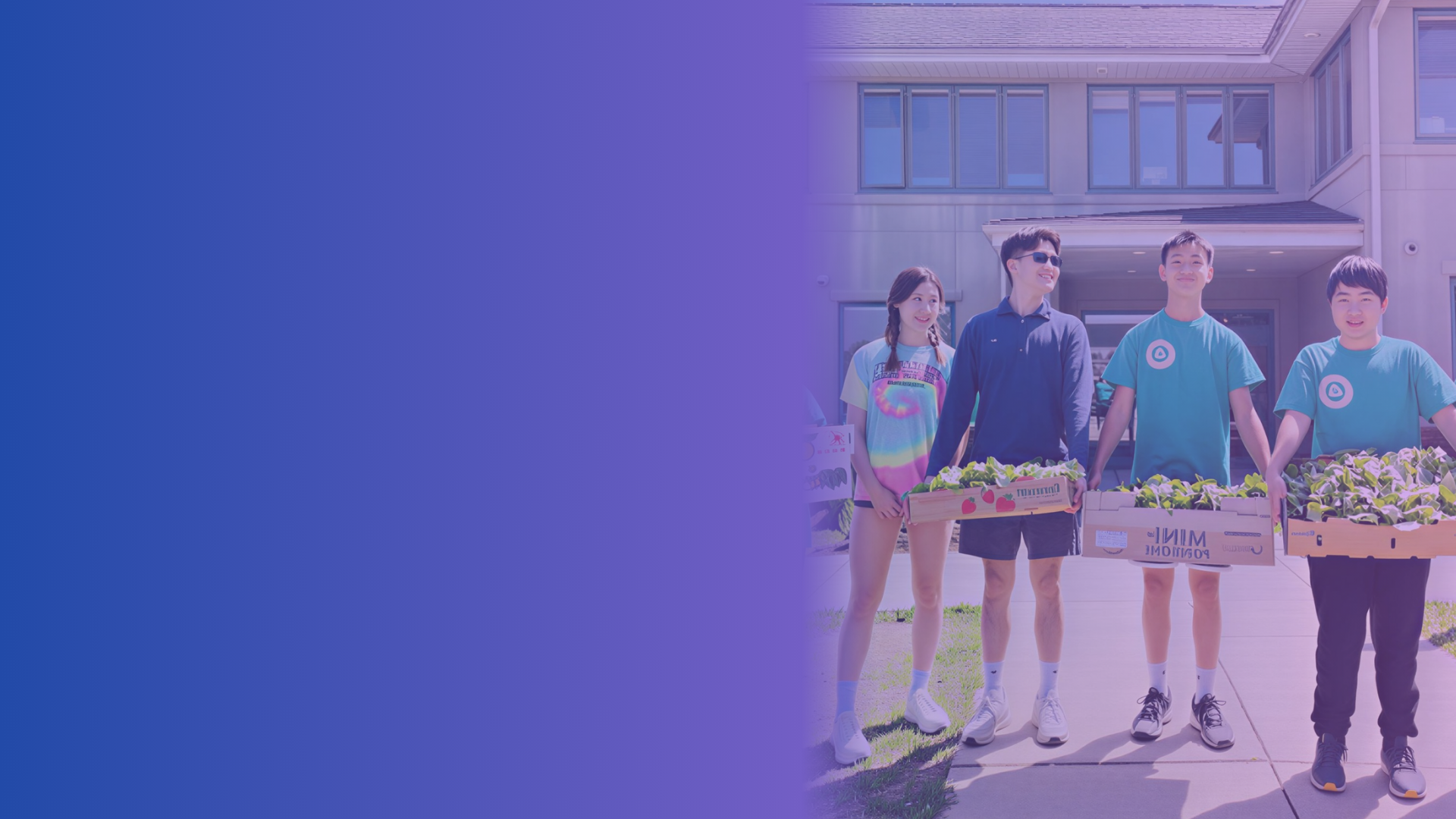 Group of four young people holding boxes of vegetables in front of a modern house during daytime