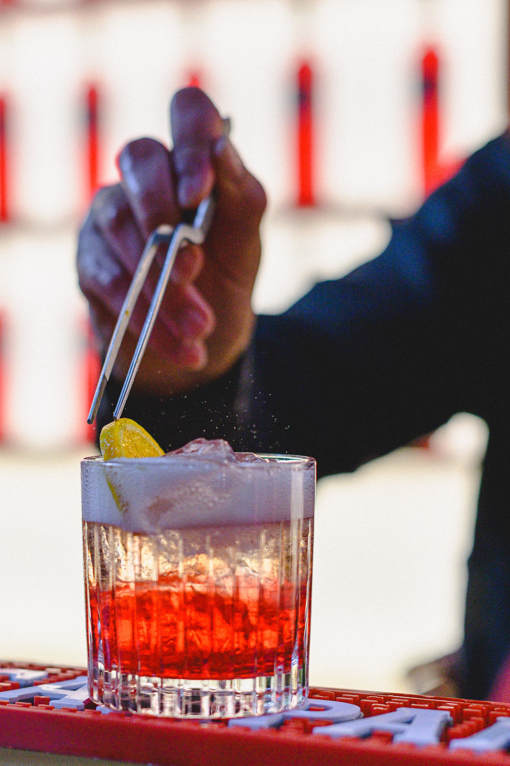 A person adding salt to a cocktail with lemon wedge using tongs, garnished with ice and salt rim in a glass.