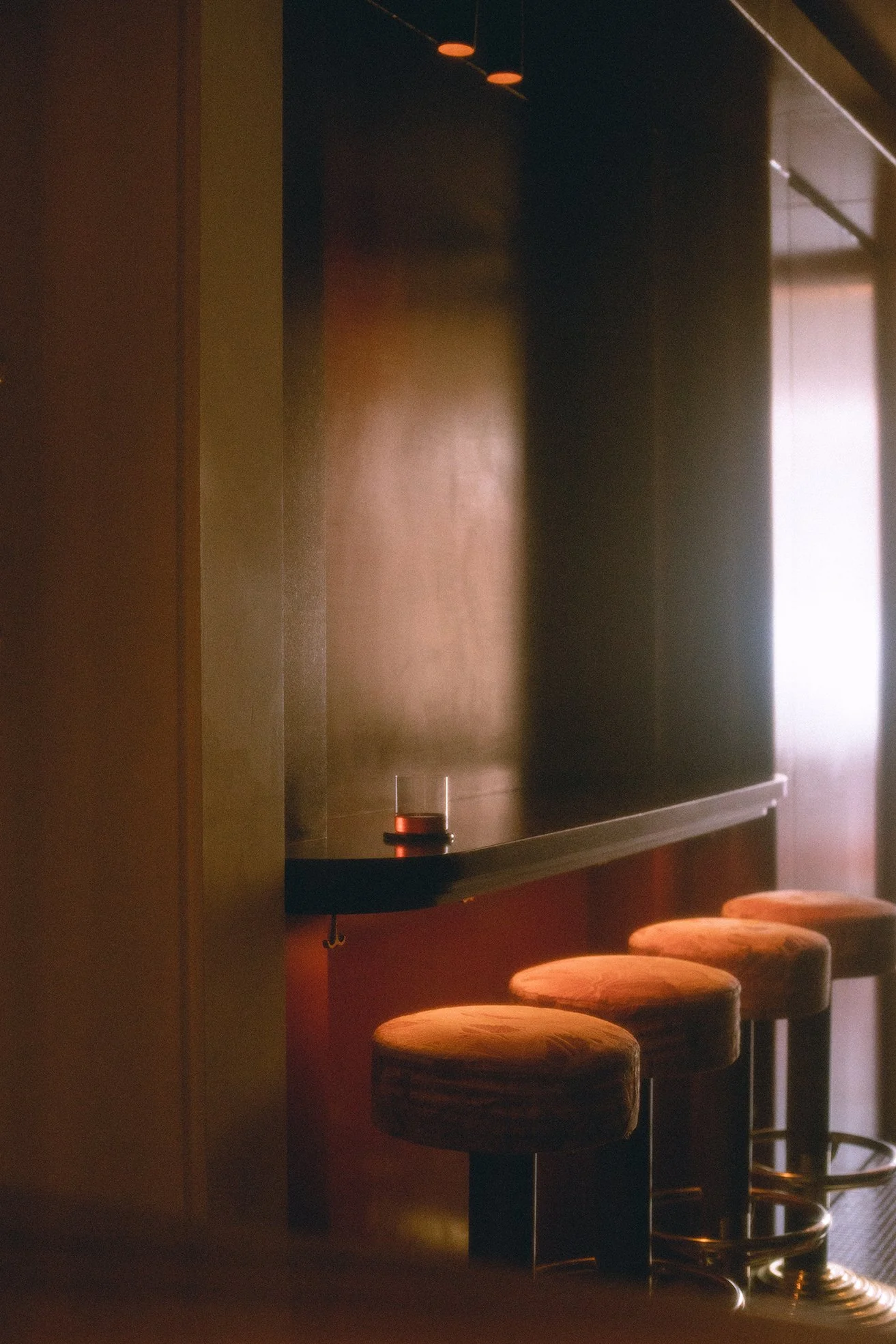 Empty bar counter with three orange bar stools, a blackboard with a small lamp, and warm lighting in a dimly lit room.