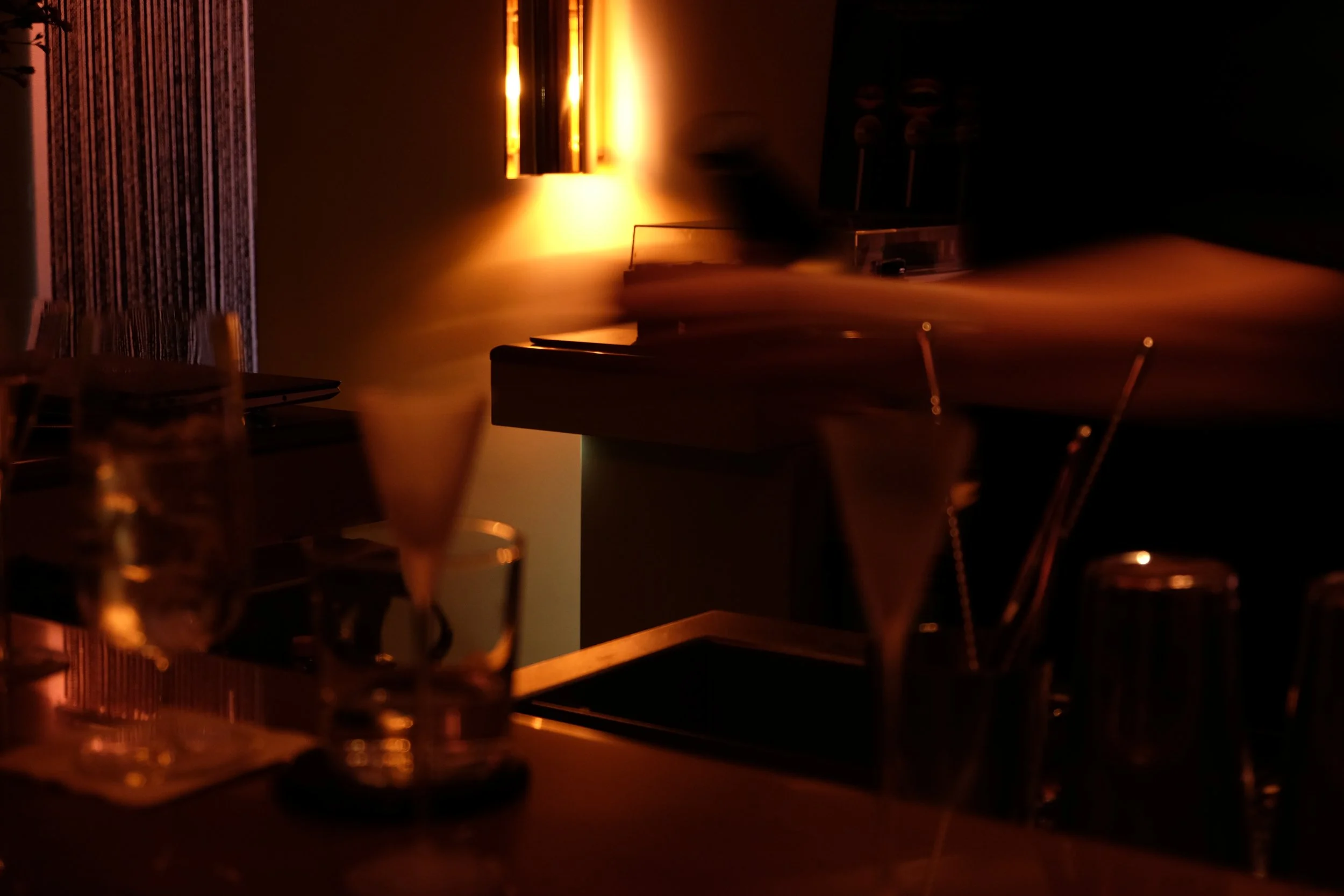 Dimly lit restaurant or bar with glasses and a piano in the background, illuminated by a warm light.