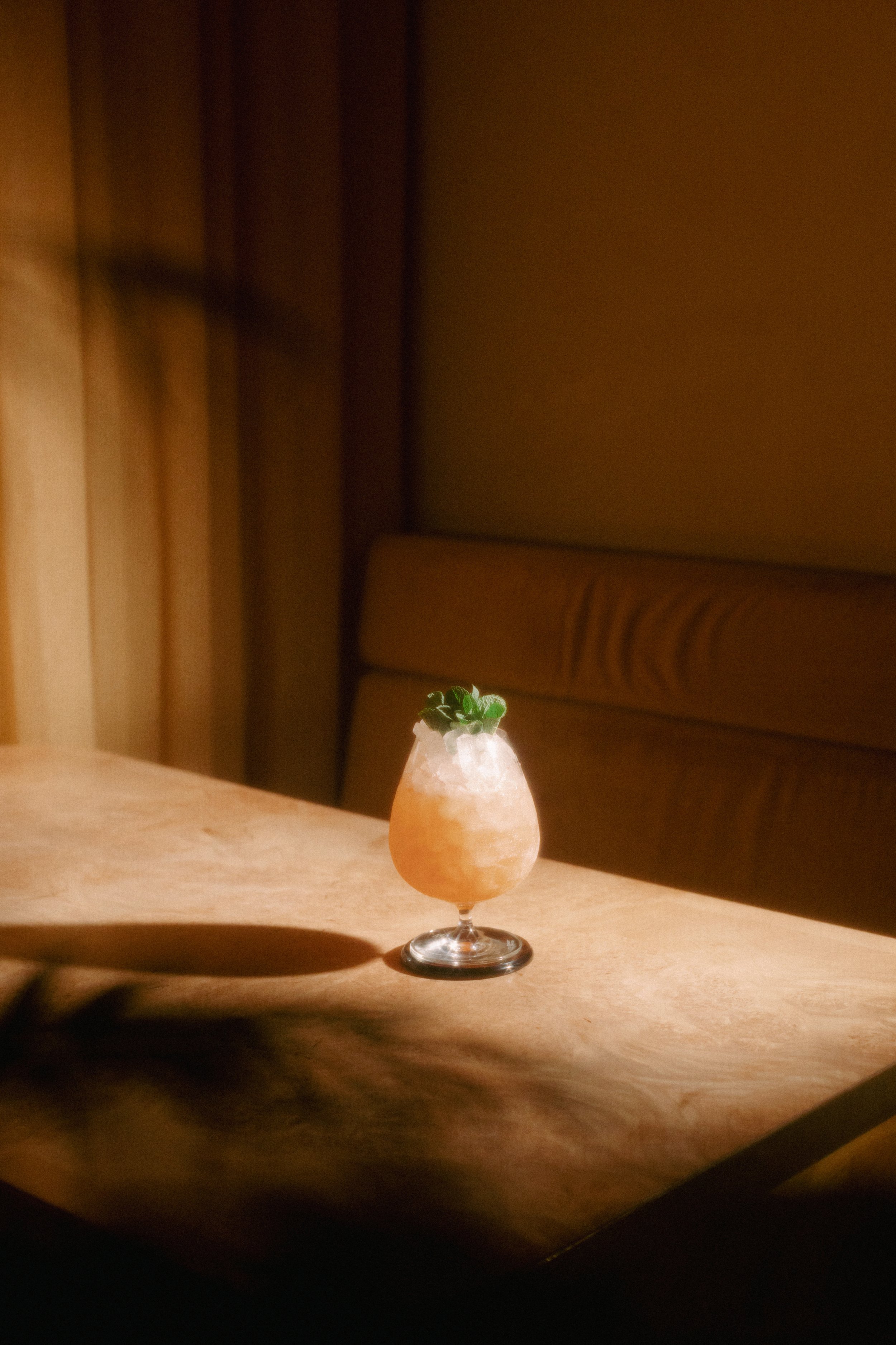 A cocktail drink garnished with mint leaves on a wooden table in a dimly lit setting.
