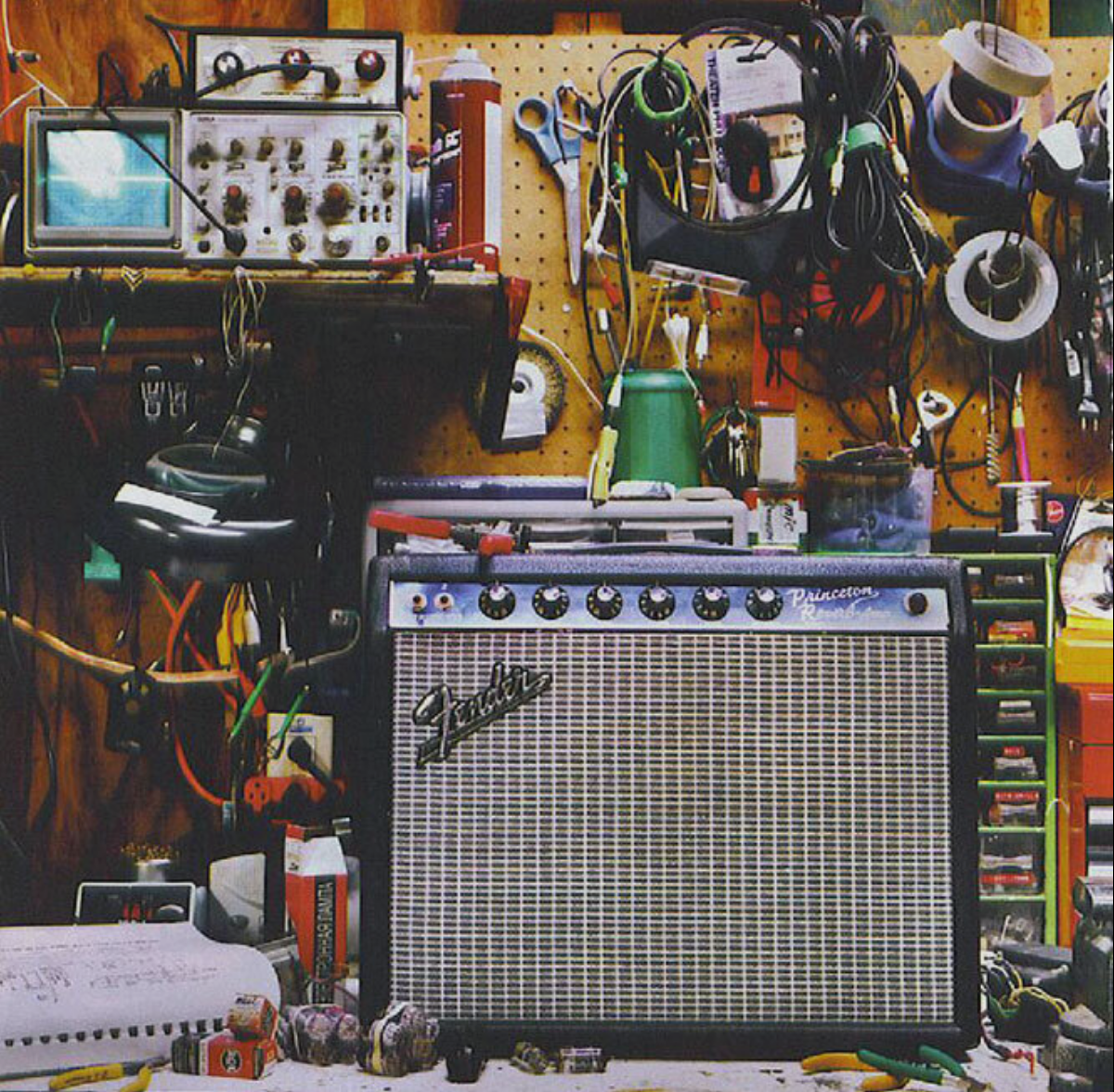 Workshop with guitar amplifier, tools, wires, and electronic equipment arranged on a pegboard and workbench.
