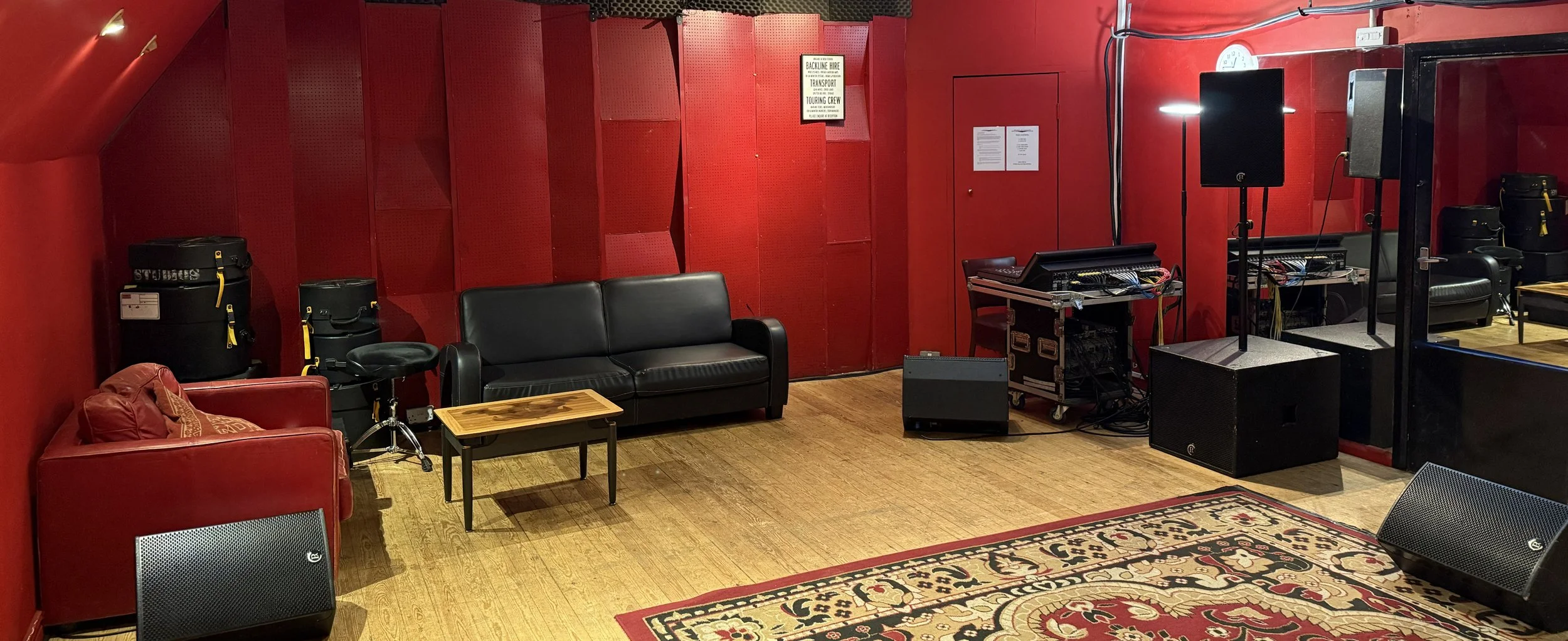 Room with red walls, wooden floor, black and red furniture, sound equipment, speakers, and a patterned rug.