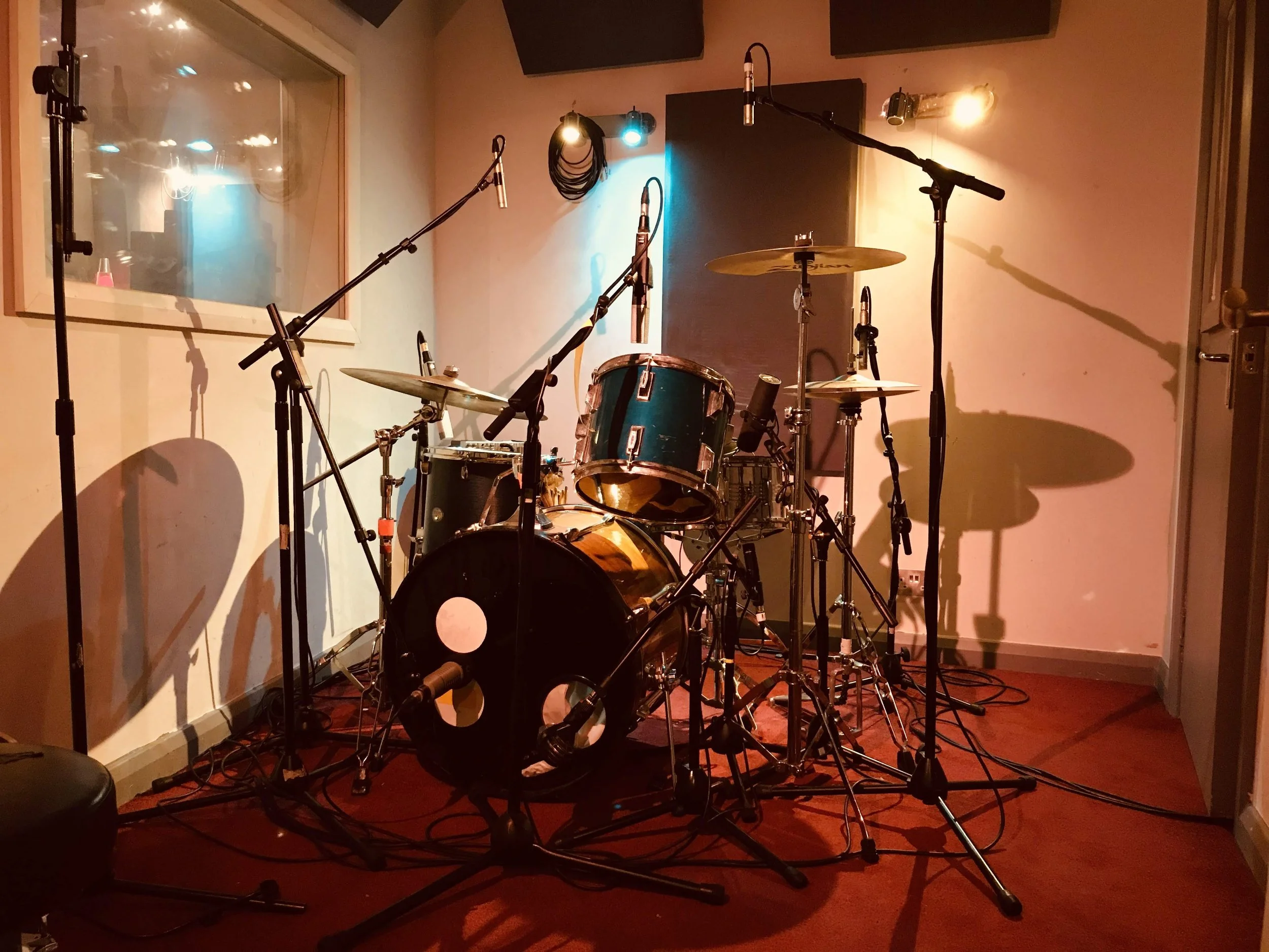 Tracking room showing drum kit and window to control room