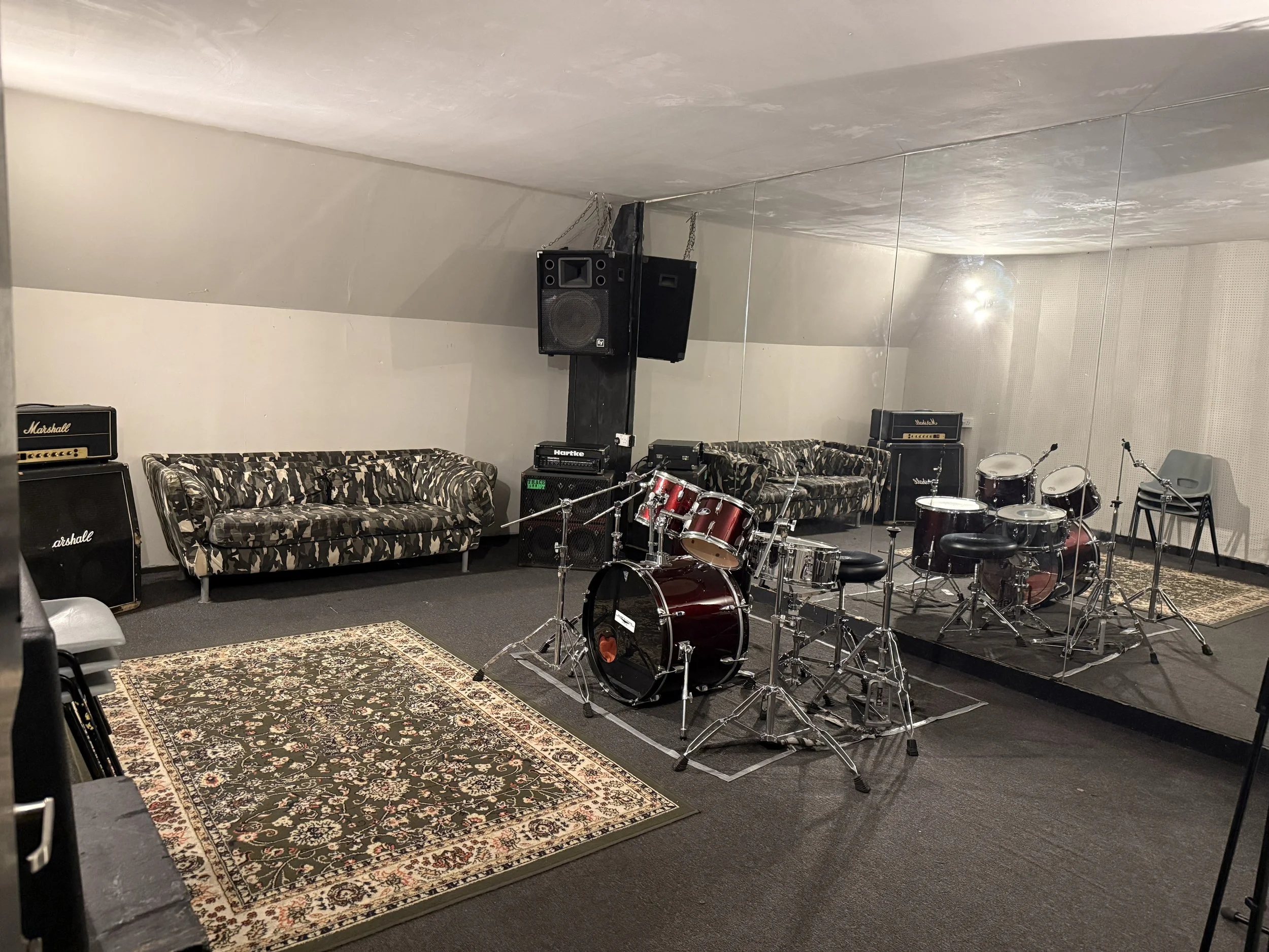 Music practice room with drums, amplifiers, microphones and acoustic panels, mirror, and rugs.