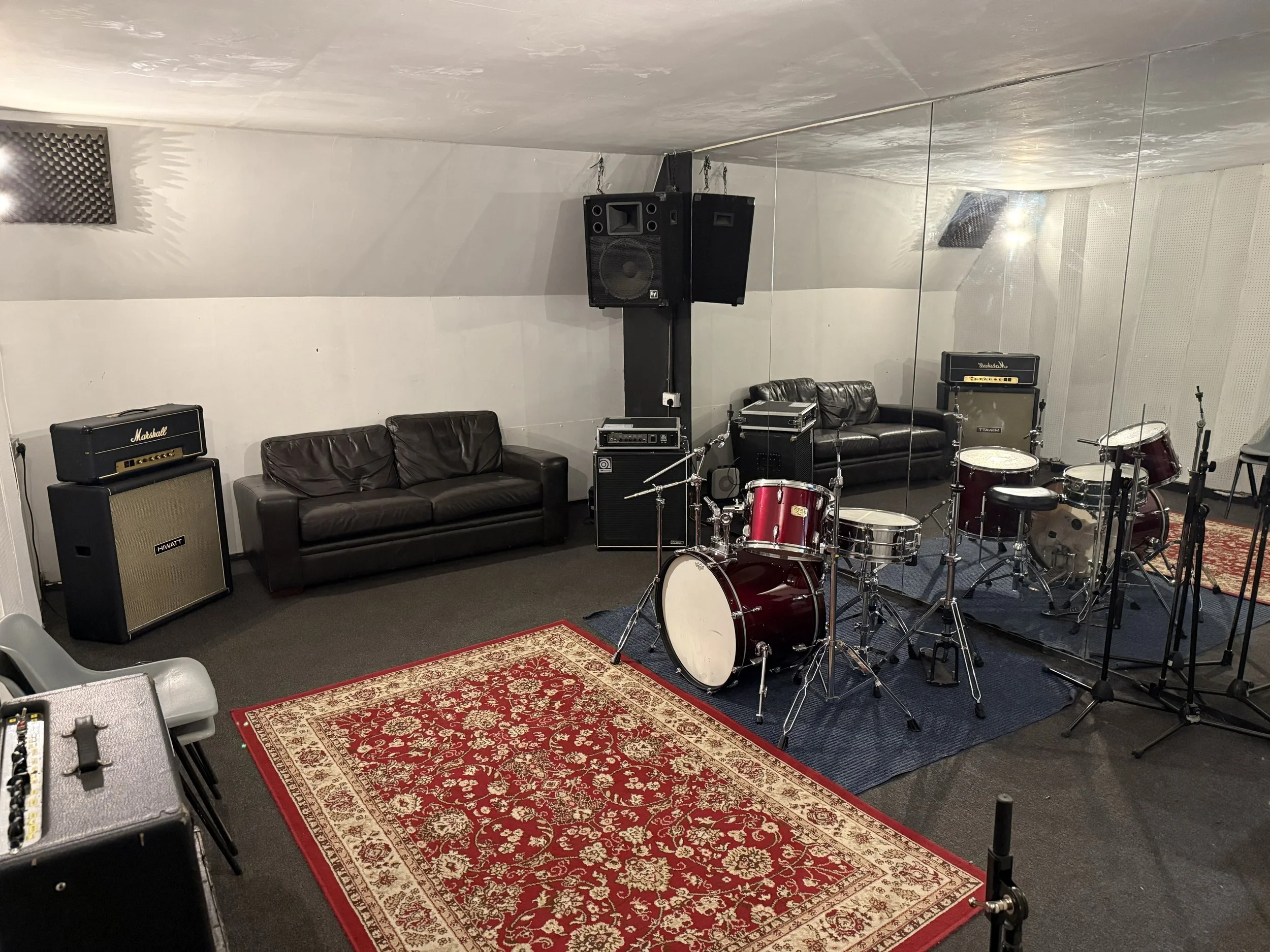 Music practice room with drums, amplifiers, microphones, and acoustic panels, mirror, and rugs.