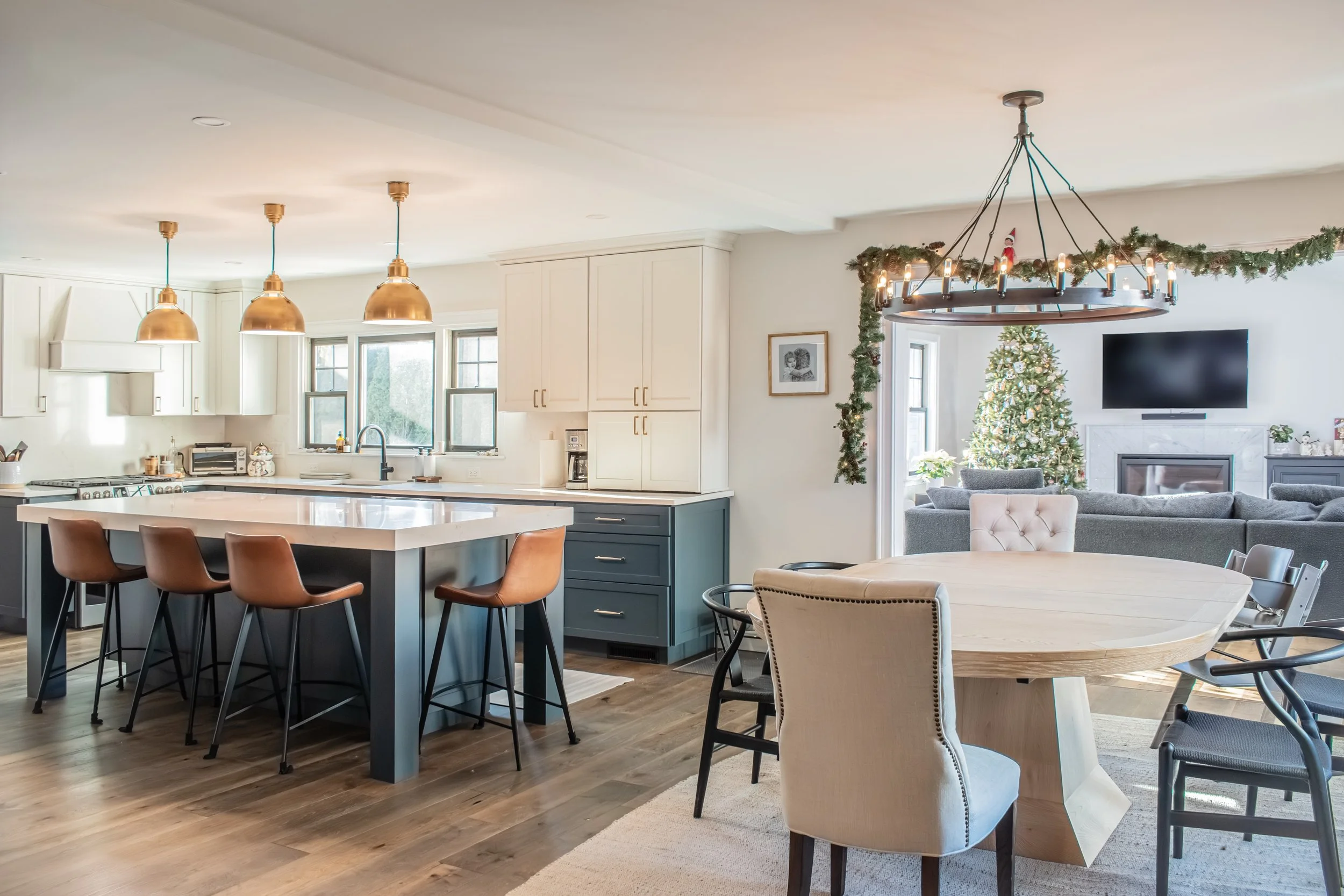 Open-concept kitchen and dining area decorated for Christmas with a Christmas tree, garland, and a chandelier.