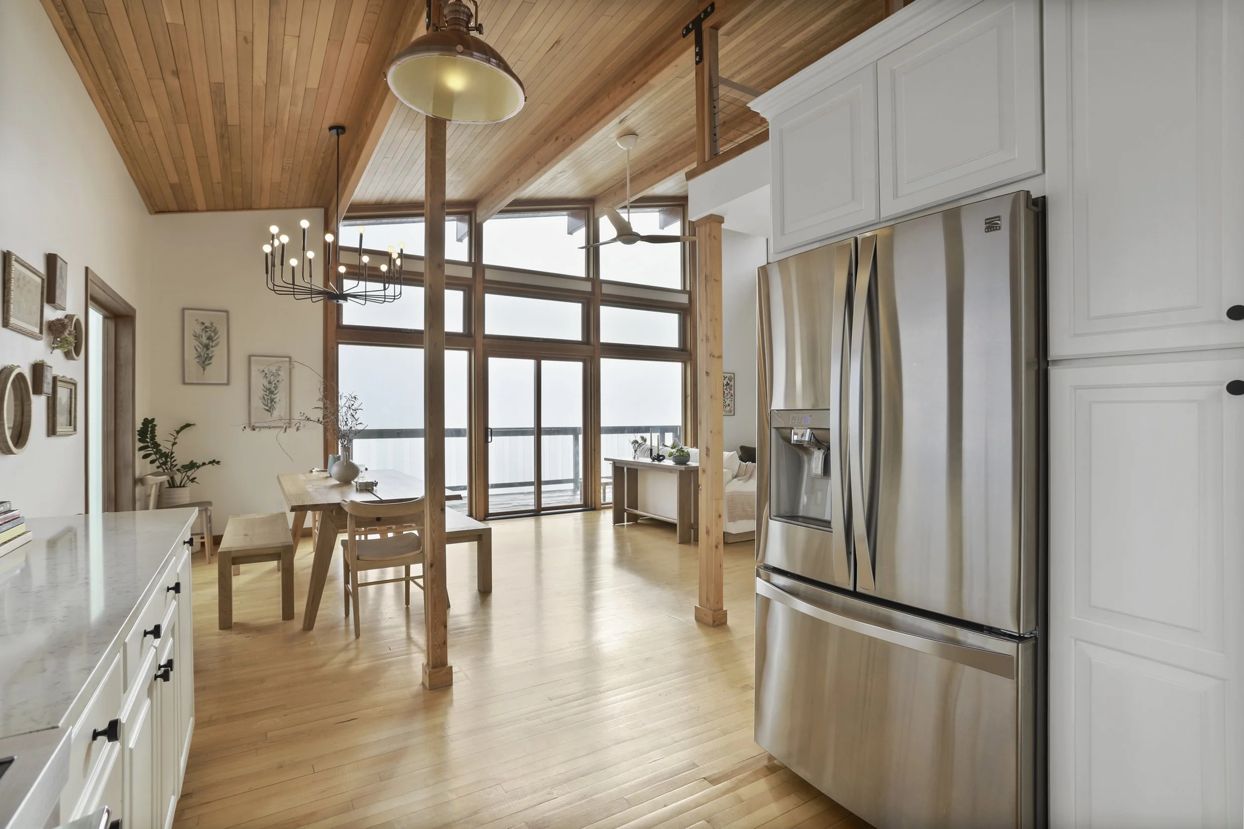 Open-concept kitchen and dining area with wood accents, white cabinetry, stainless steel refrigerator, and large windows