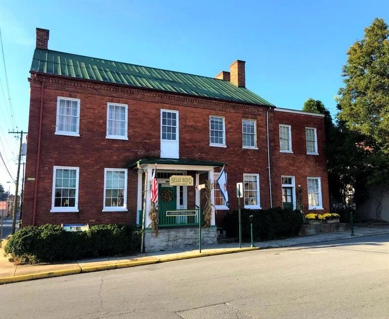 A three-story brick building with a green metal roof, decorated with flags and a sign that reads 'Belle Boyd.'