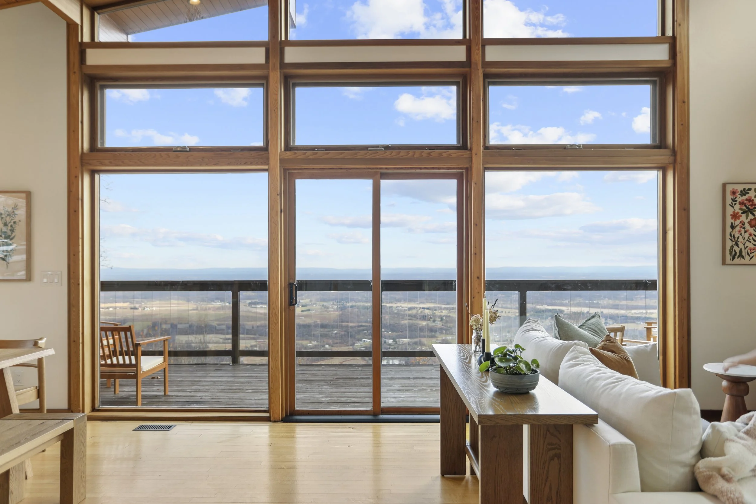 Living room with large wooden-framed glass sliding doors leading to a balcony with outdoor seating and a view of the sky and landscape