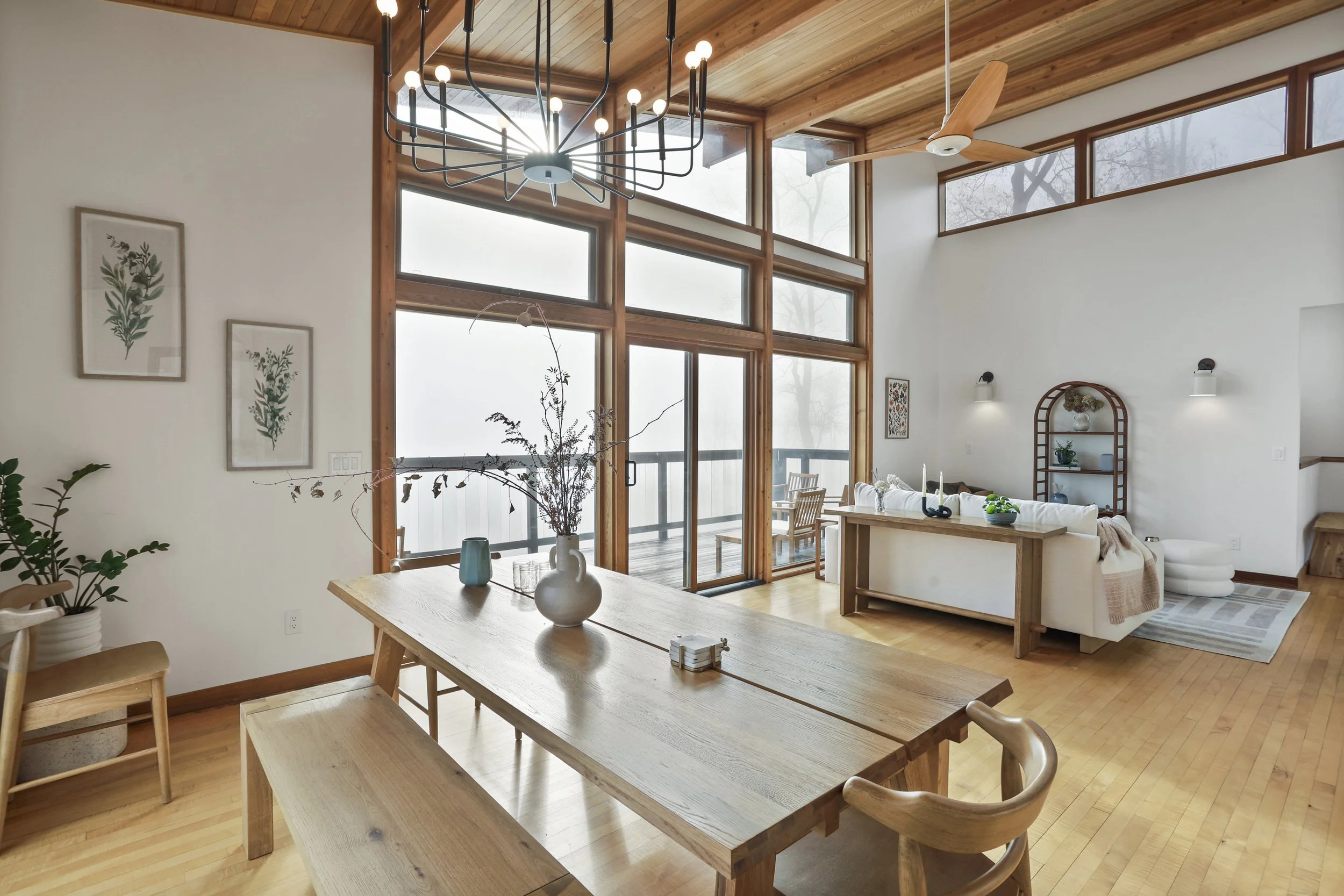 Open-concept living and dining room with large windows, wood accents, a chandelier, and minimal decor.