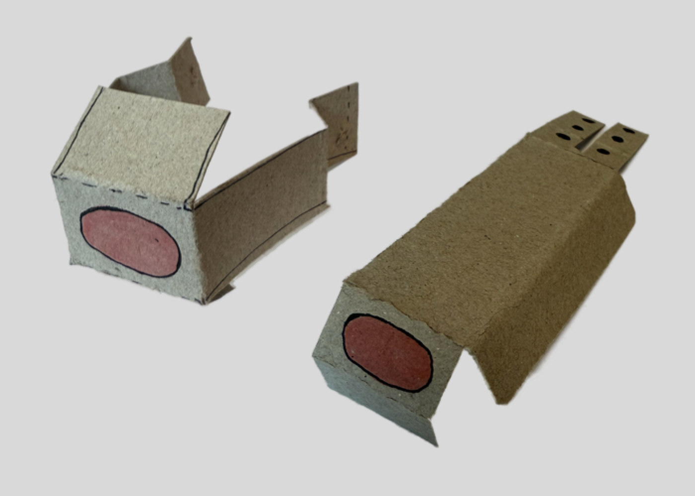 Two small cardboard models of battery lock ideas with red oval lights on one side, they show the two different original ideas, on a plain light background.