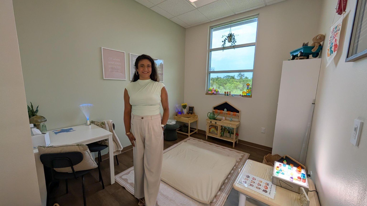Kristy Guetzloe in her Sproutlings occupational therapy room, with a movement mat, play kitchen, and light table