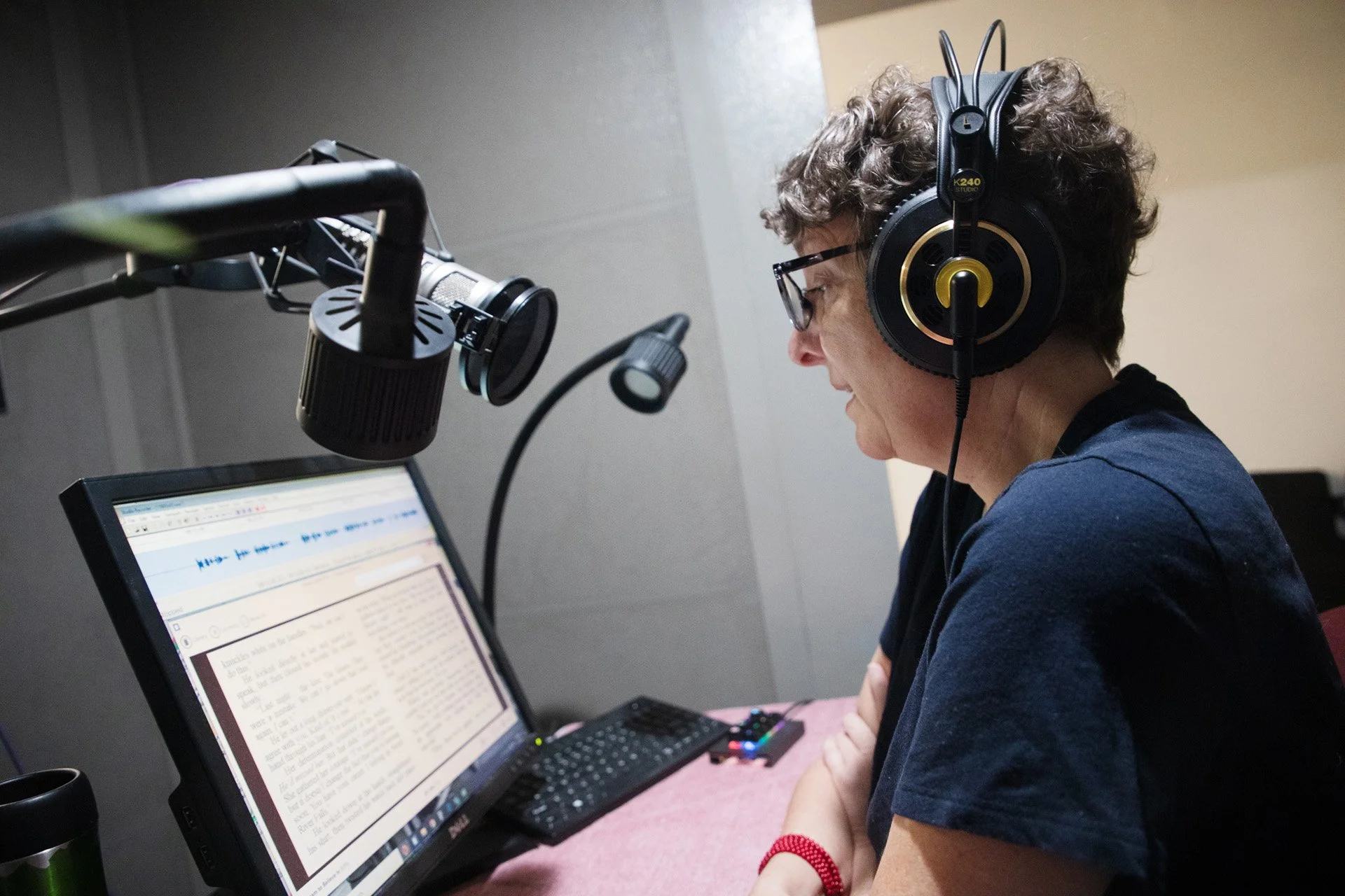 A person is resting their arms on a table while looking at words on a computer screen and talking into a microphone.