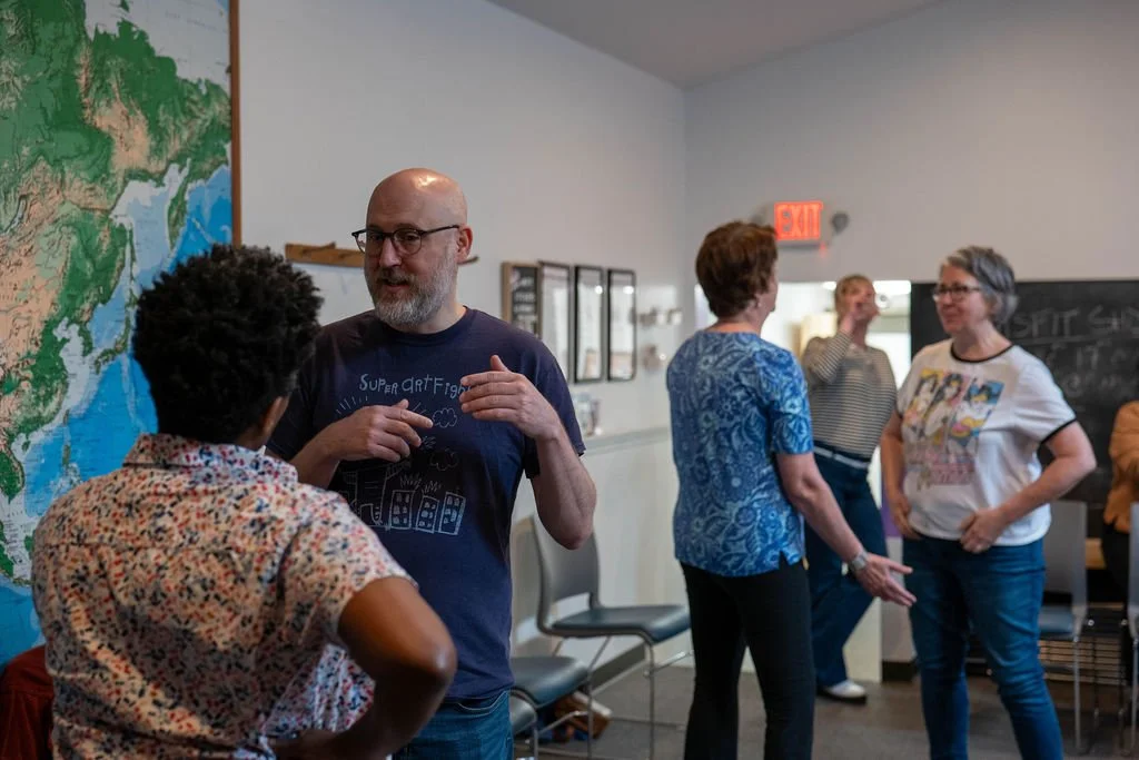 A group of five adults engaging in conversation in a room with a large map on the wall.