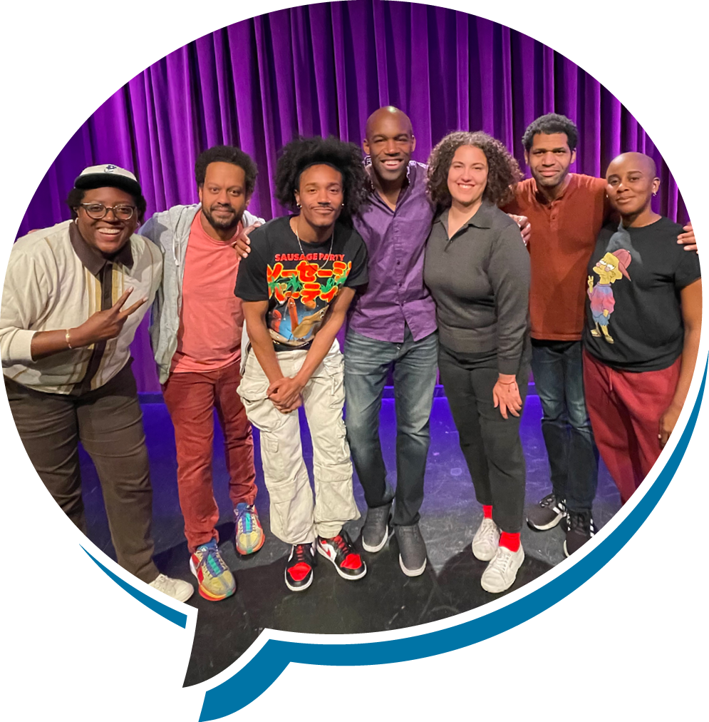 A group of eight diverse people standing on a stage with purple curtains, smiling and posing for the photo.