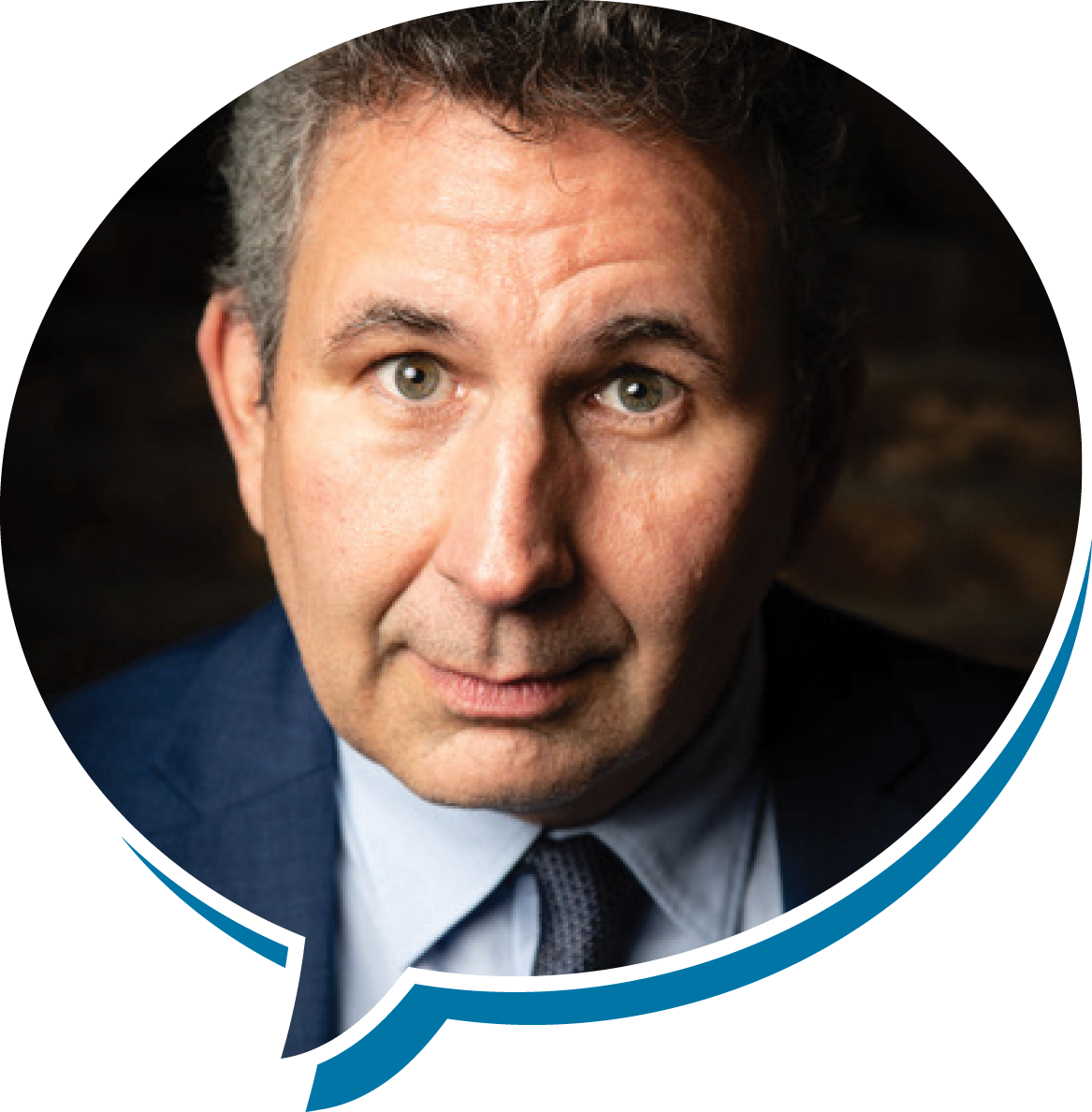 Close-up of a man in a suit with blue eyes and dark, wavy hair, looking at the camera with a surprised expression.
